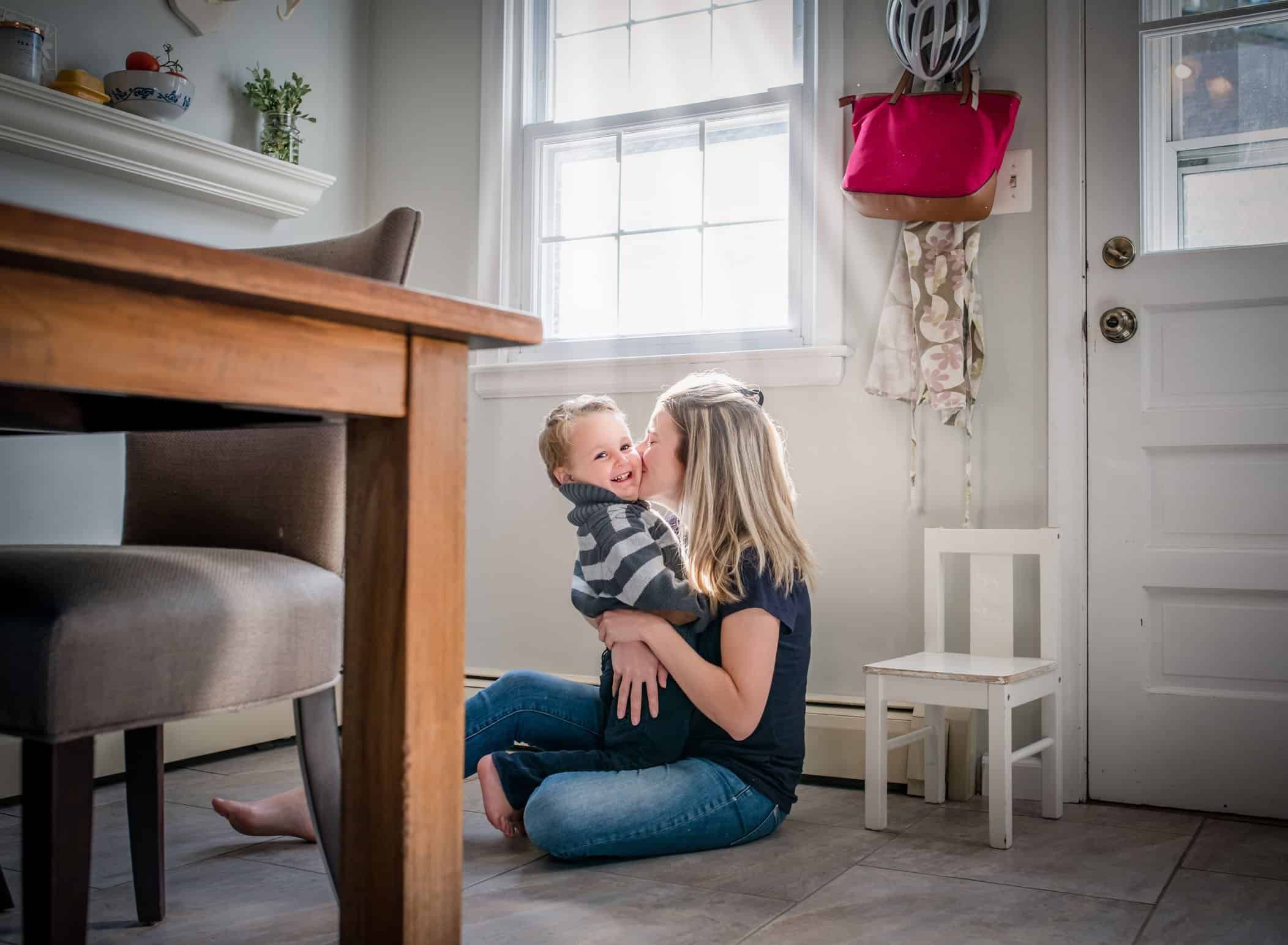 Mom kissing toddler son on cheek on kitchen floor