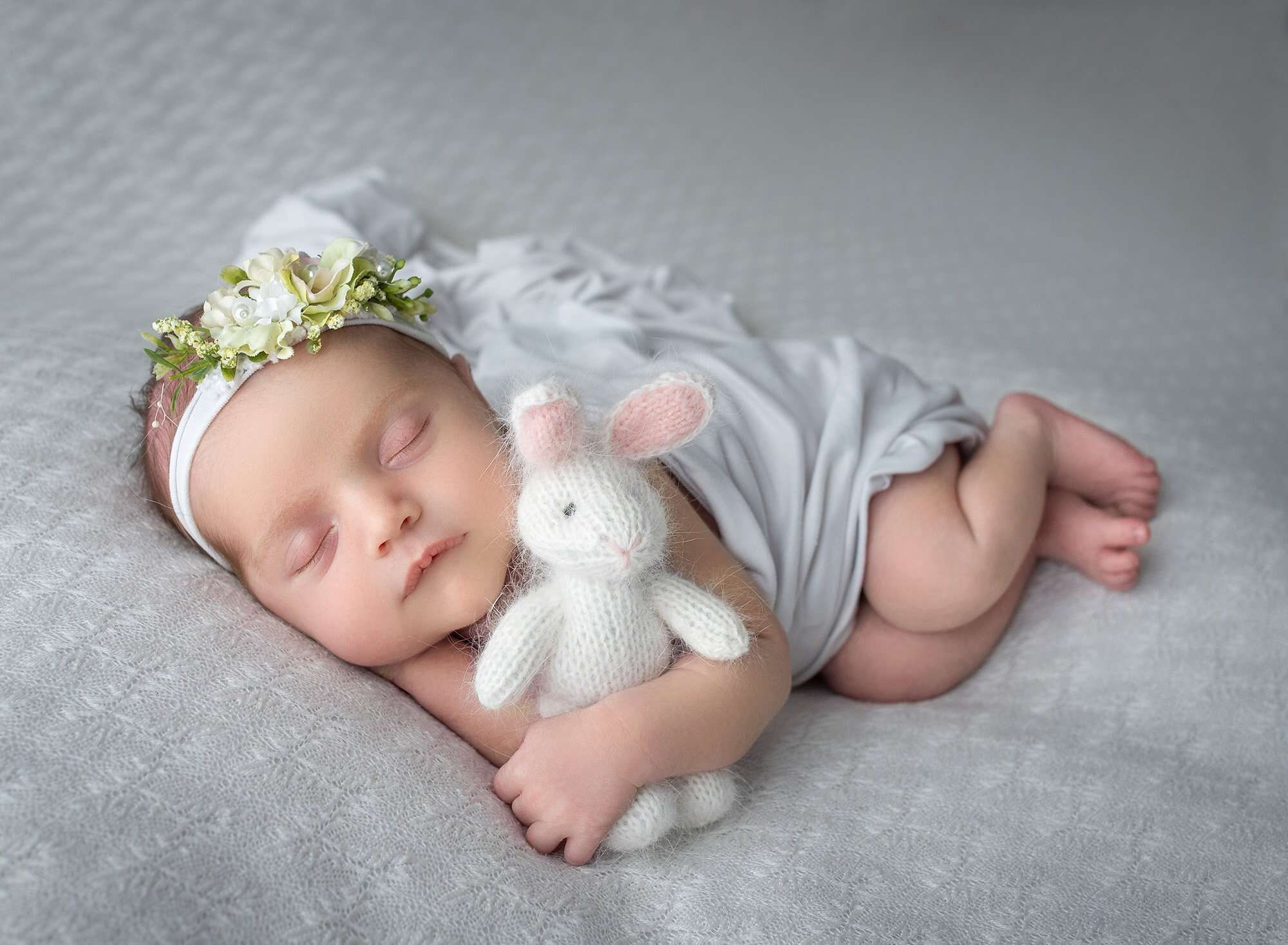 best newborn photographer newborn baby girl asleep holding fuzzy bunny with white blanket draped over her