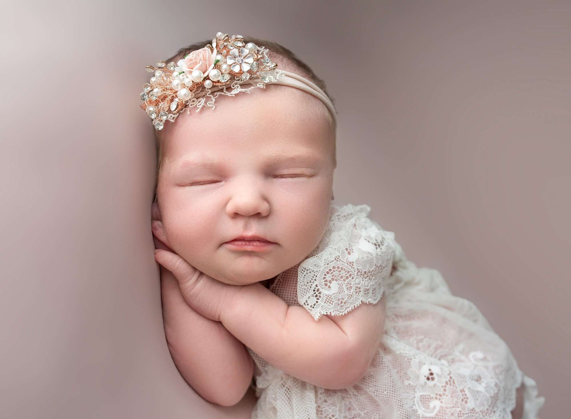 stunning newborn baby girl asleep on her hands wearing a white laced dress