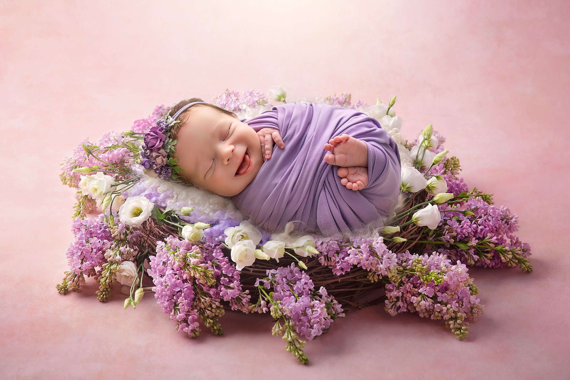 newborn photography in CT smiling newborn swaddled and sleeping in a nest of lilacs