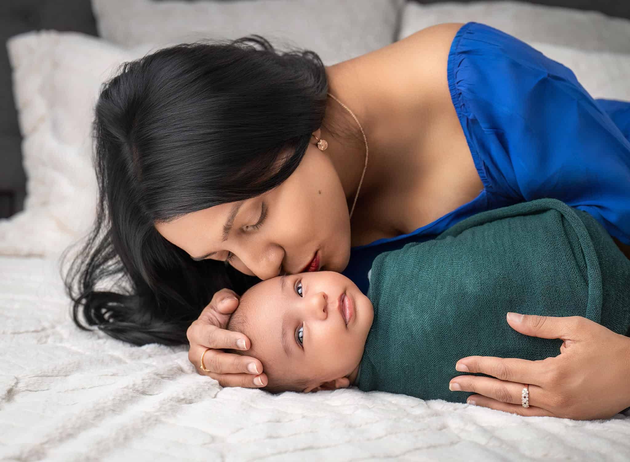 Mom leaning down to kiss newborn baby's cheek