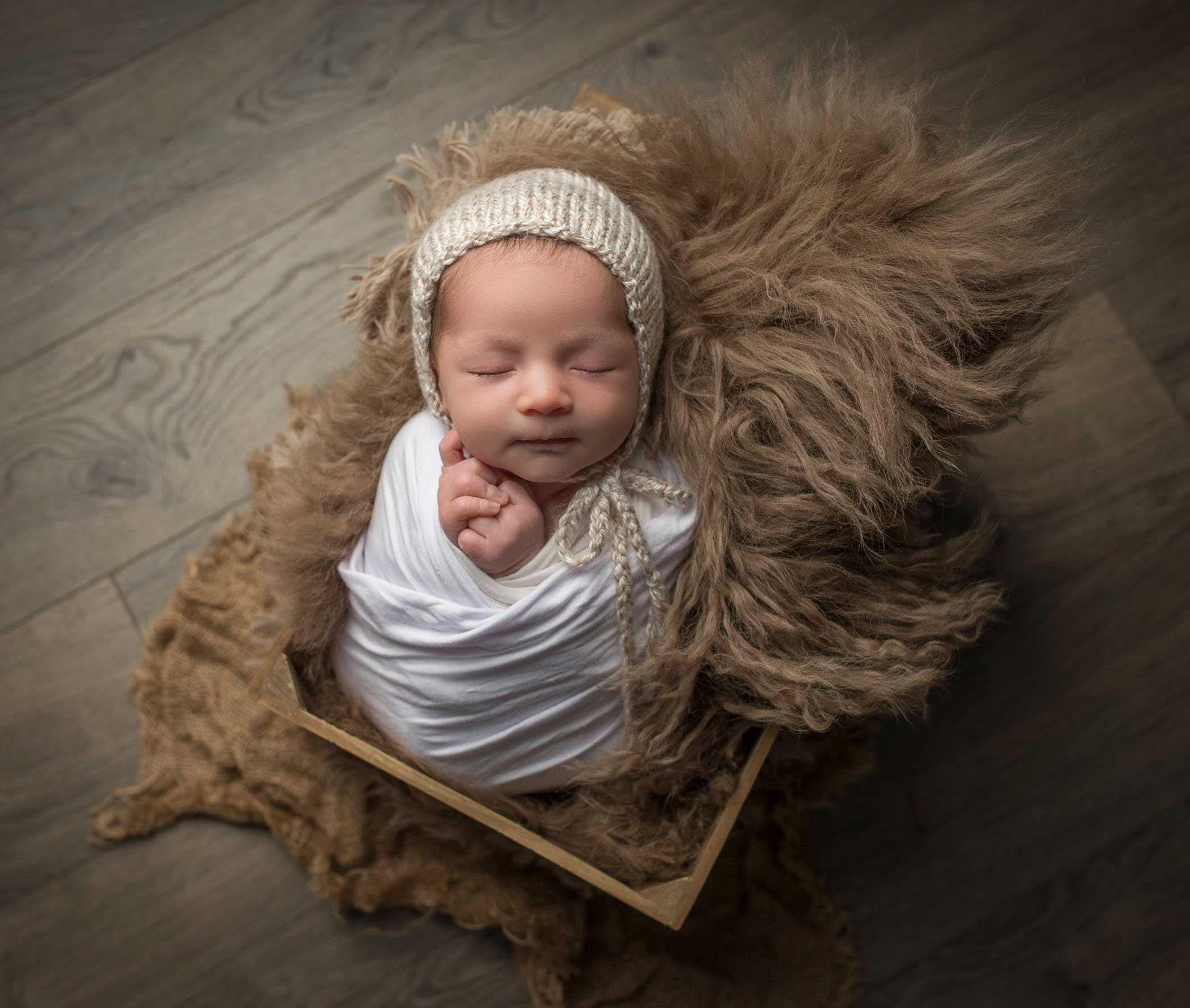 newborn baby boy asleep in crate on wood floor