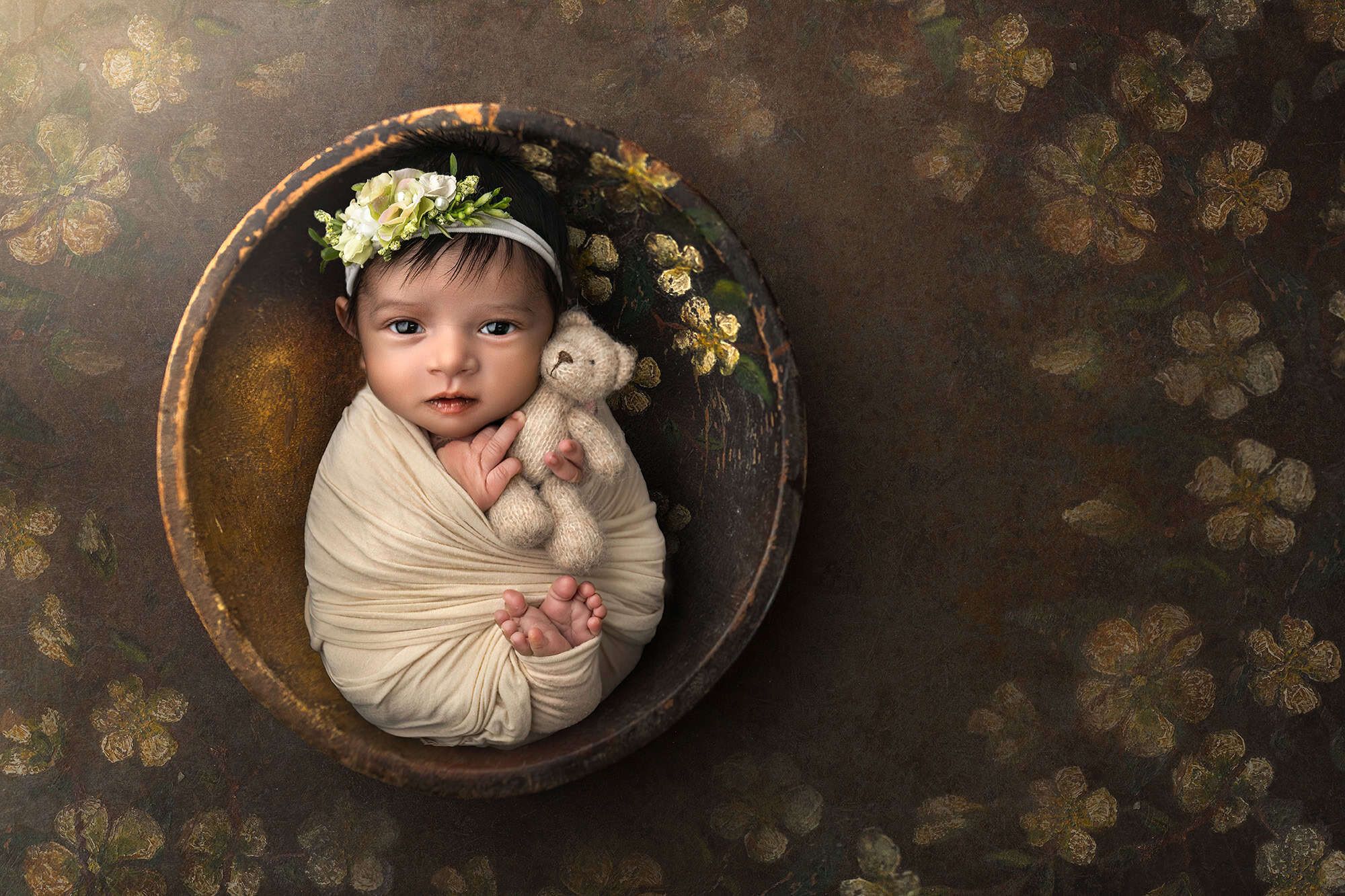 newborn photographer safely posed baby during photo session cuddling a teddy bear in a rustic bowl with gold flowers