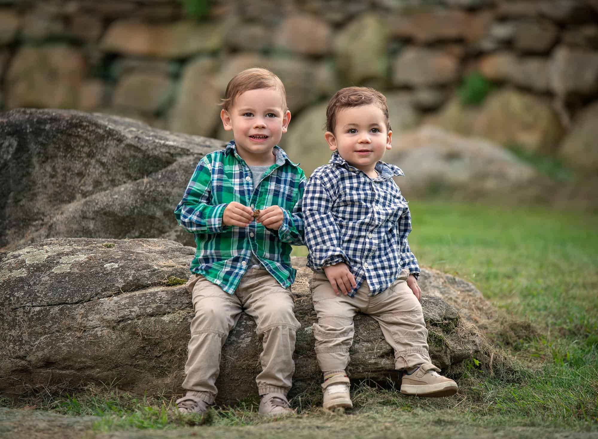 two young brothers sitting on a large rock in nature