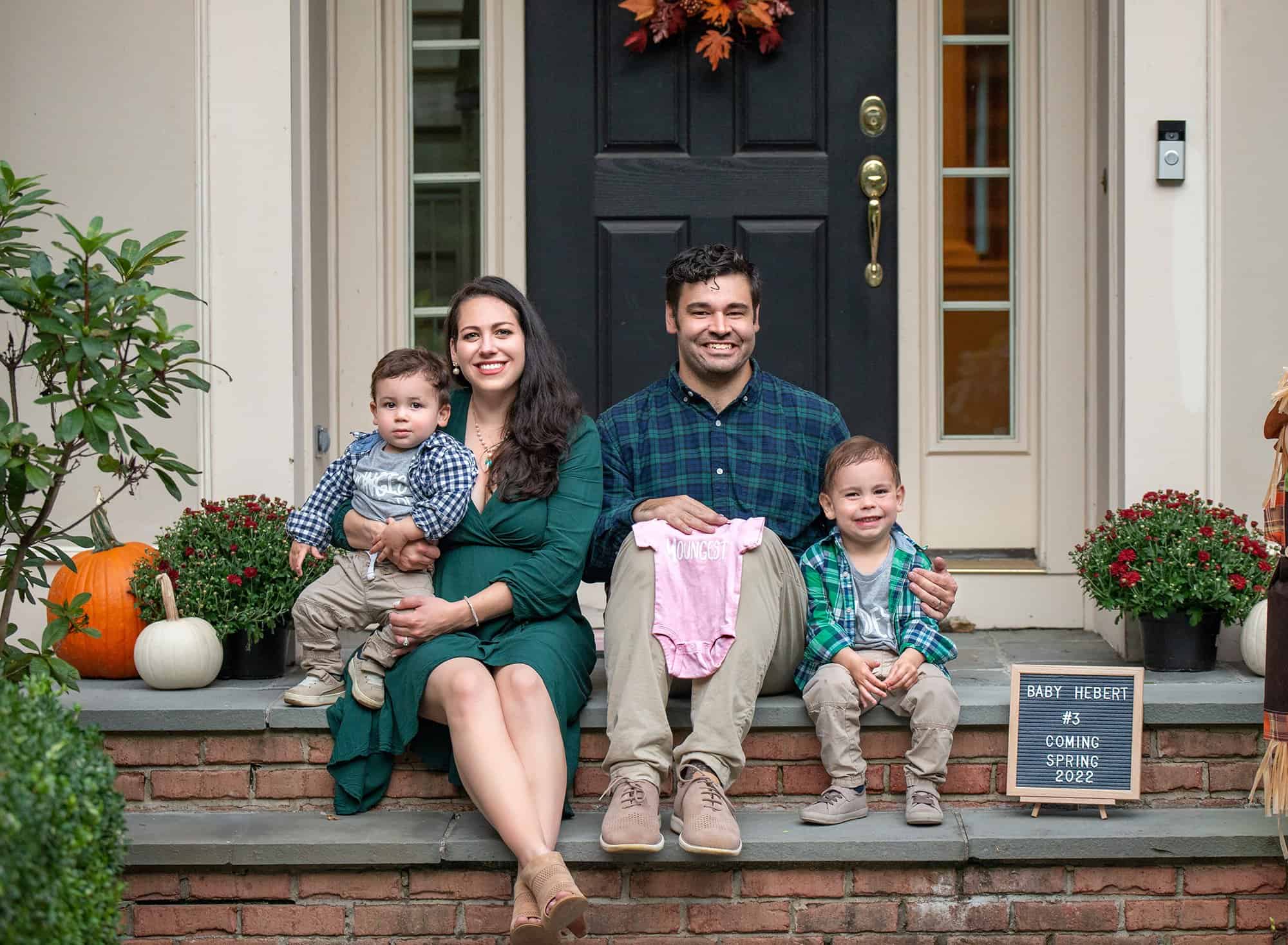 1 year old and family photography couple posing with young sons at house with a baby announcement