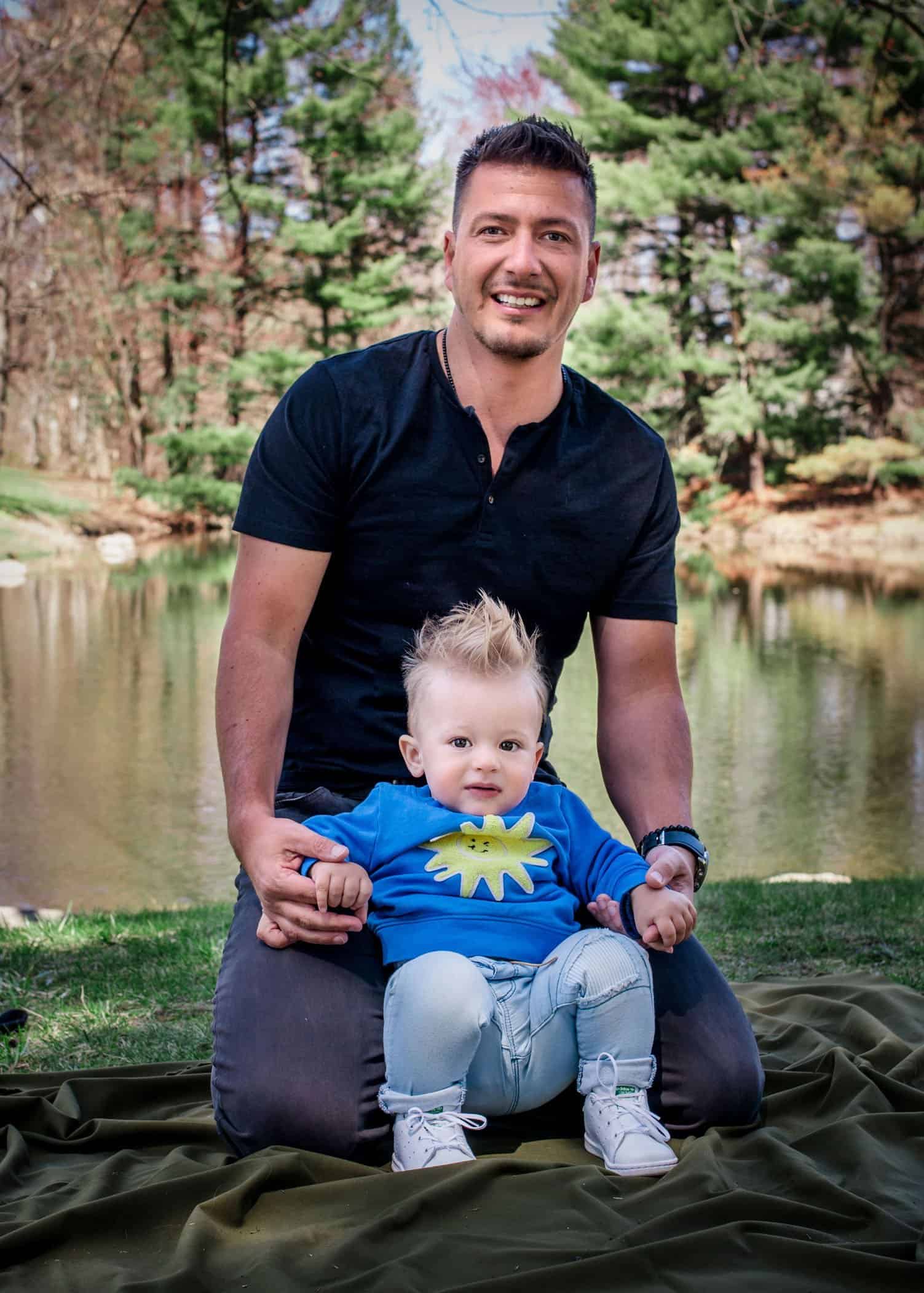Dad holding his 1 year old boy on his knees in front of pond