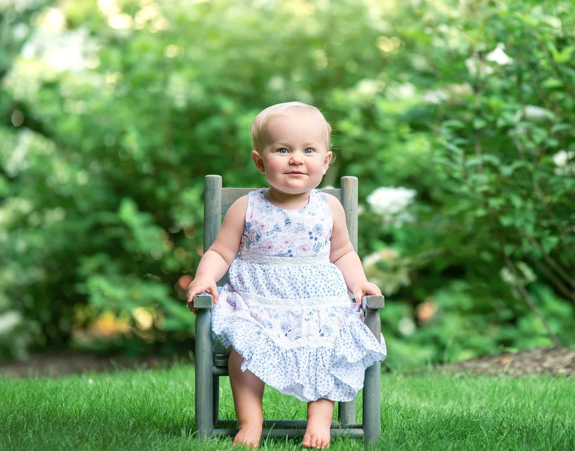 one year old little girl sitting on rustic chair in nature