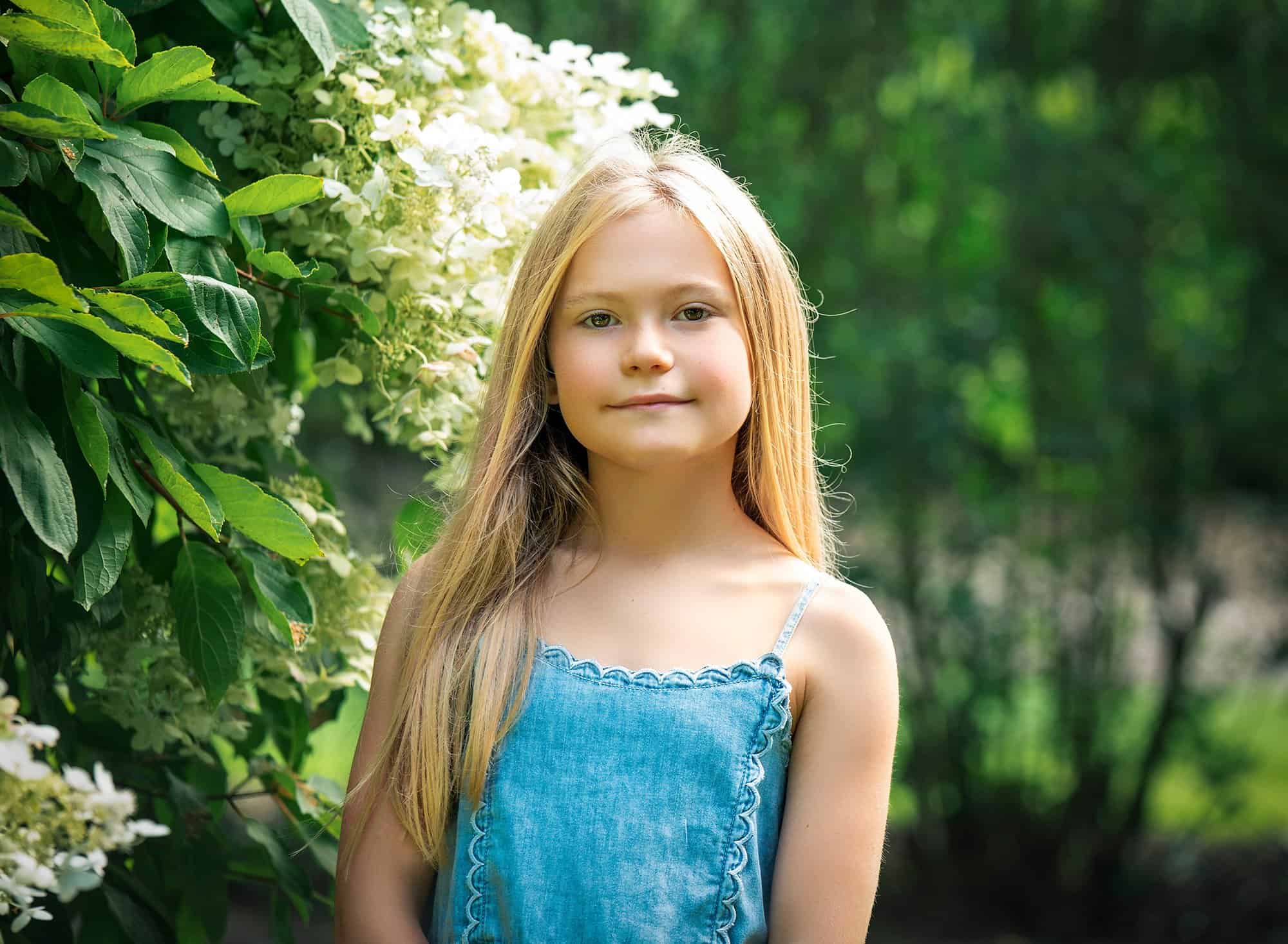 blonde haired girl posing in front of flower bush