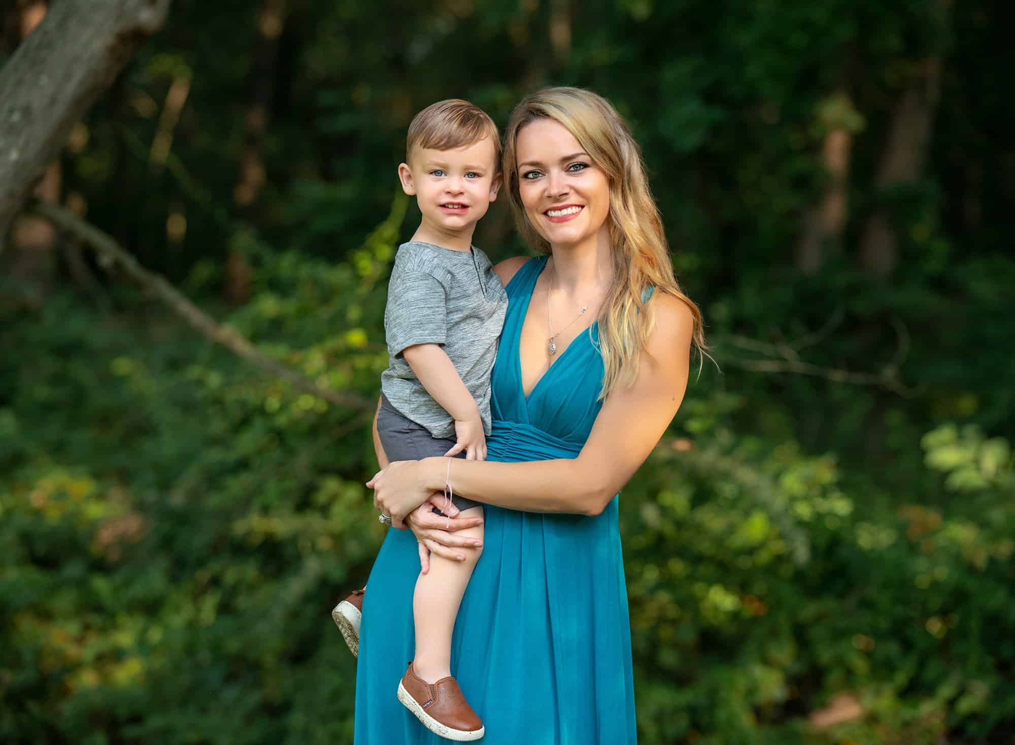 blonde mother holding two year old son in nature