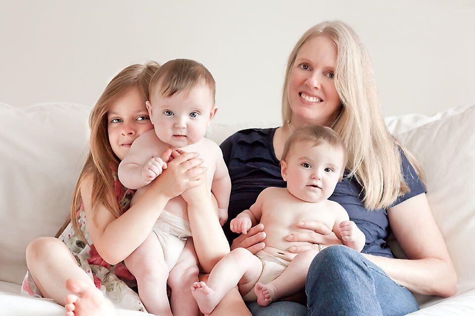 Momma and her three little kids sitting on a white couch for a portrait