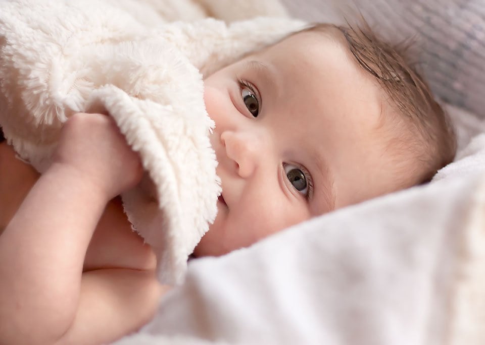 baby girl cuddled up with a white, fuzzy blanket