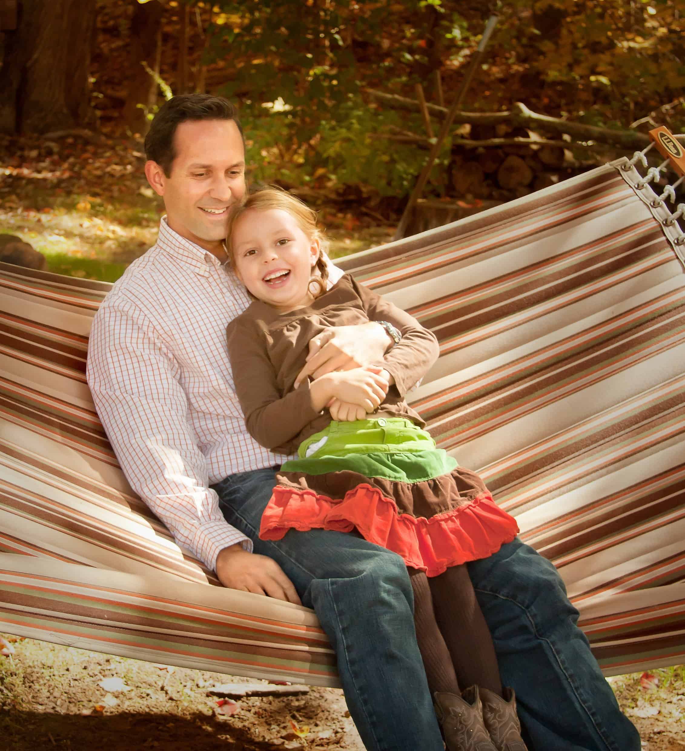 Dad and 6 year old daughter laugh and swing in a hammock
