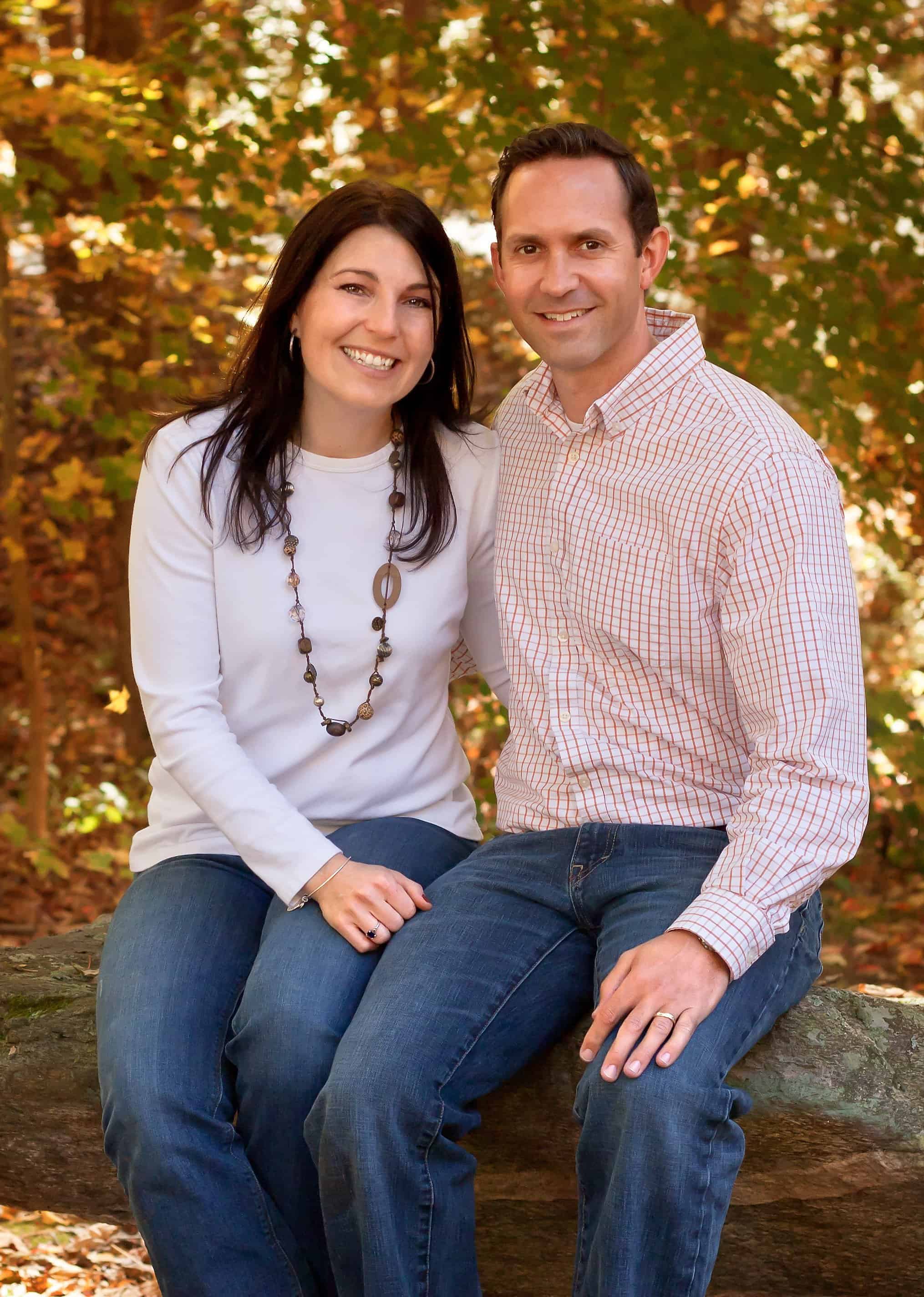 Mom and Dad sitting on a big rock with fall folliage behind them