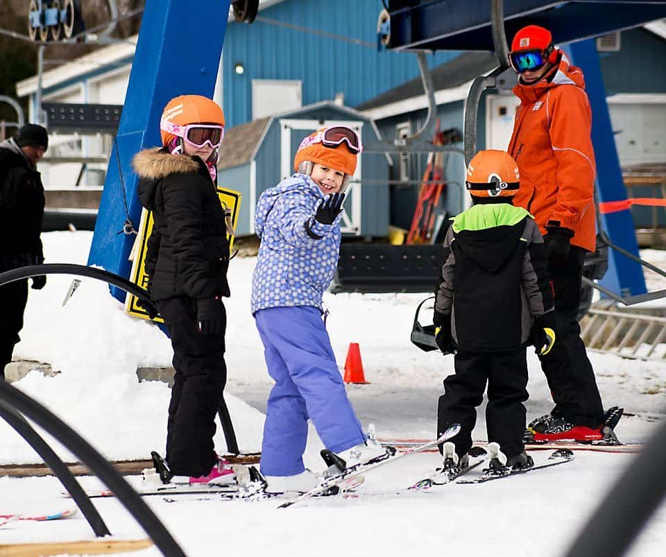 7 year old girl in bright purple getting ready to get on a ski lift with a group of other young kids