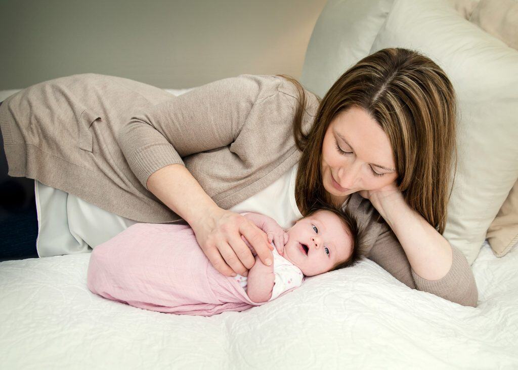 mom admiring newborn lying on bed