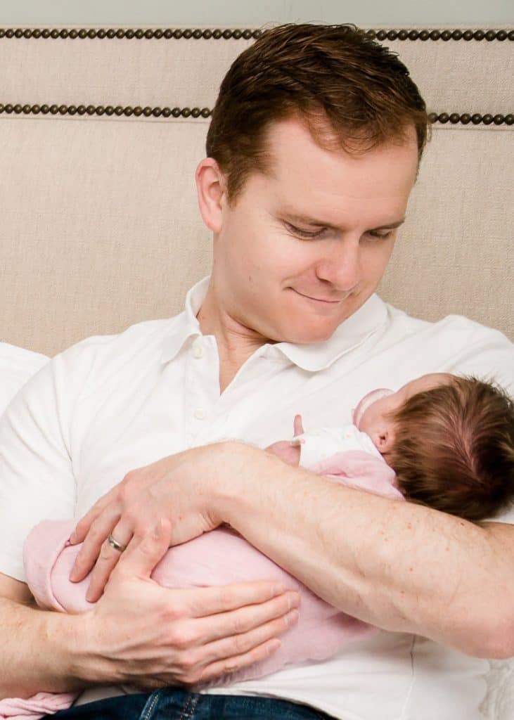 Dad holding newborn girl in his arms and smiling