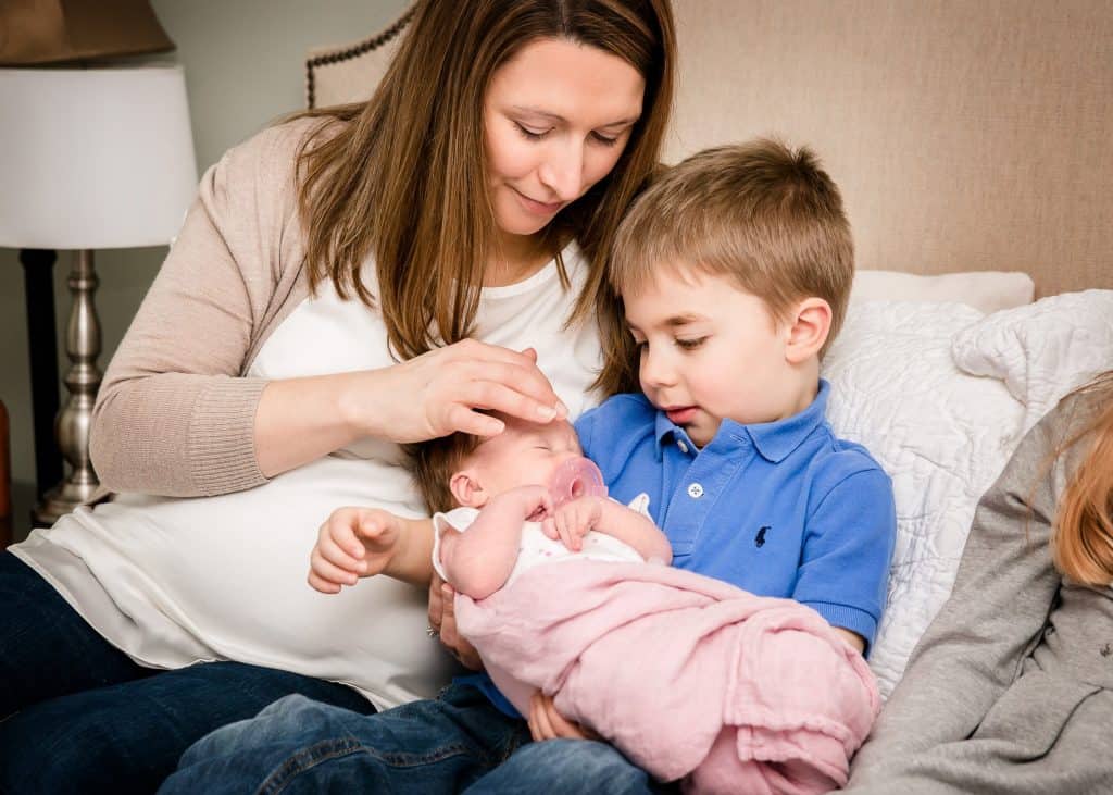 4 year old brother holds newborn sister with Mom