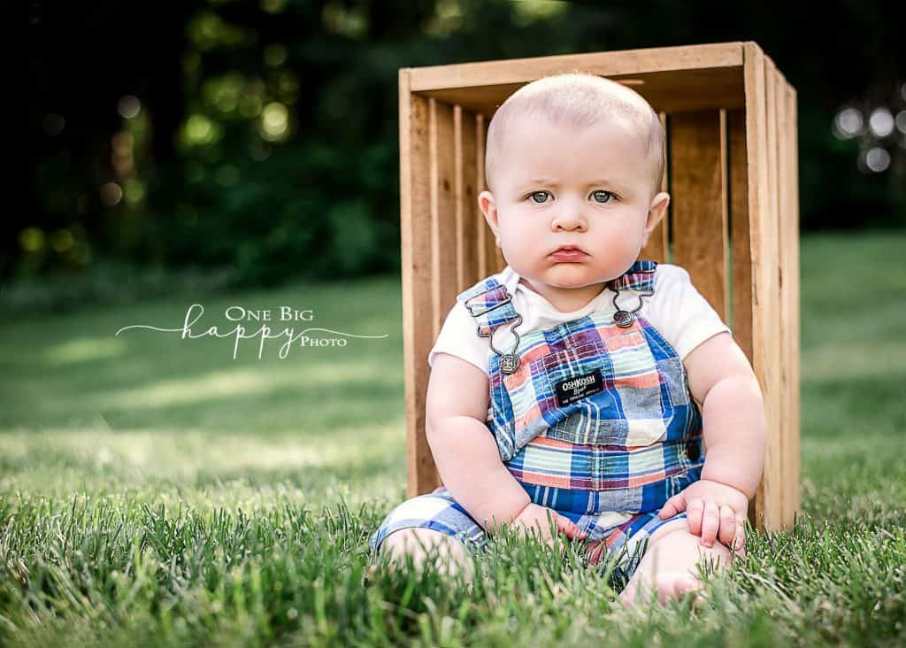 6 month old boy sitting in the grass with wooden crate behind him in summer