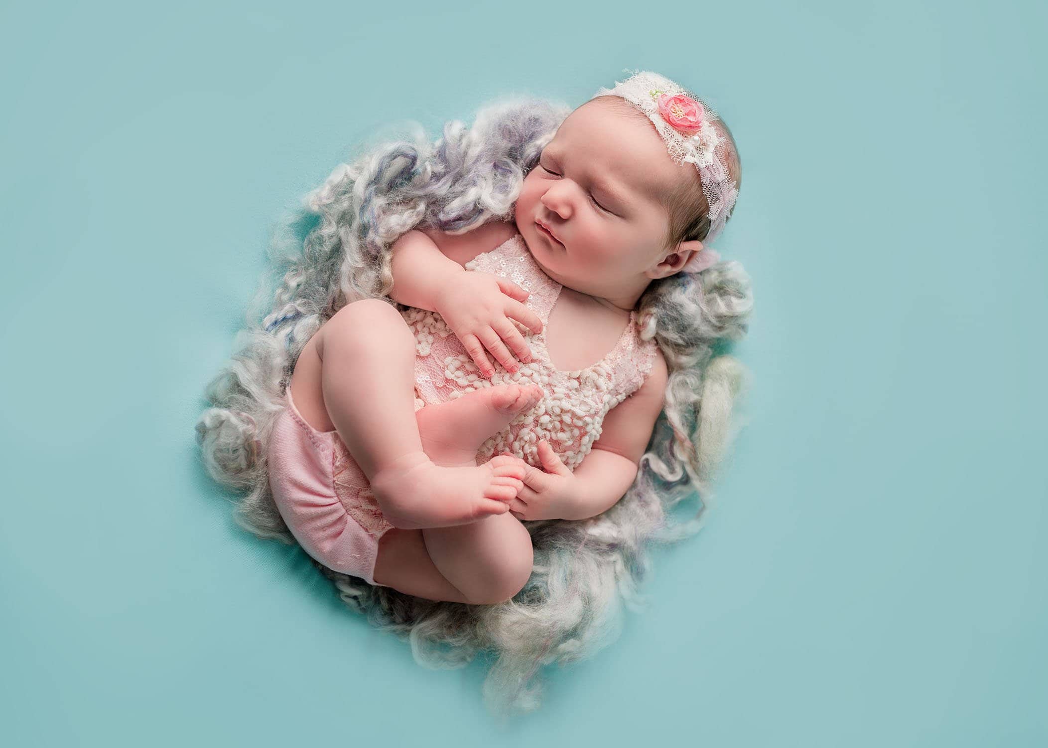 newborn baby girl in pink lace romper sleeping on teal background One Big Happy Photo
