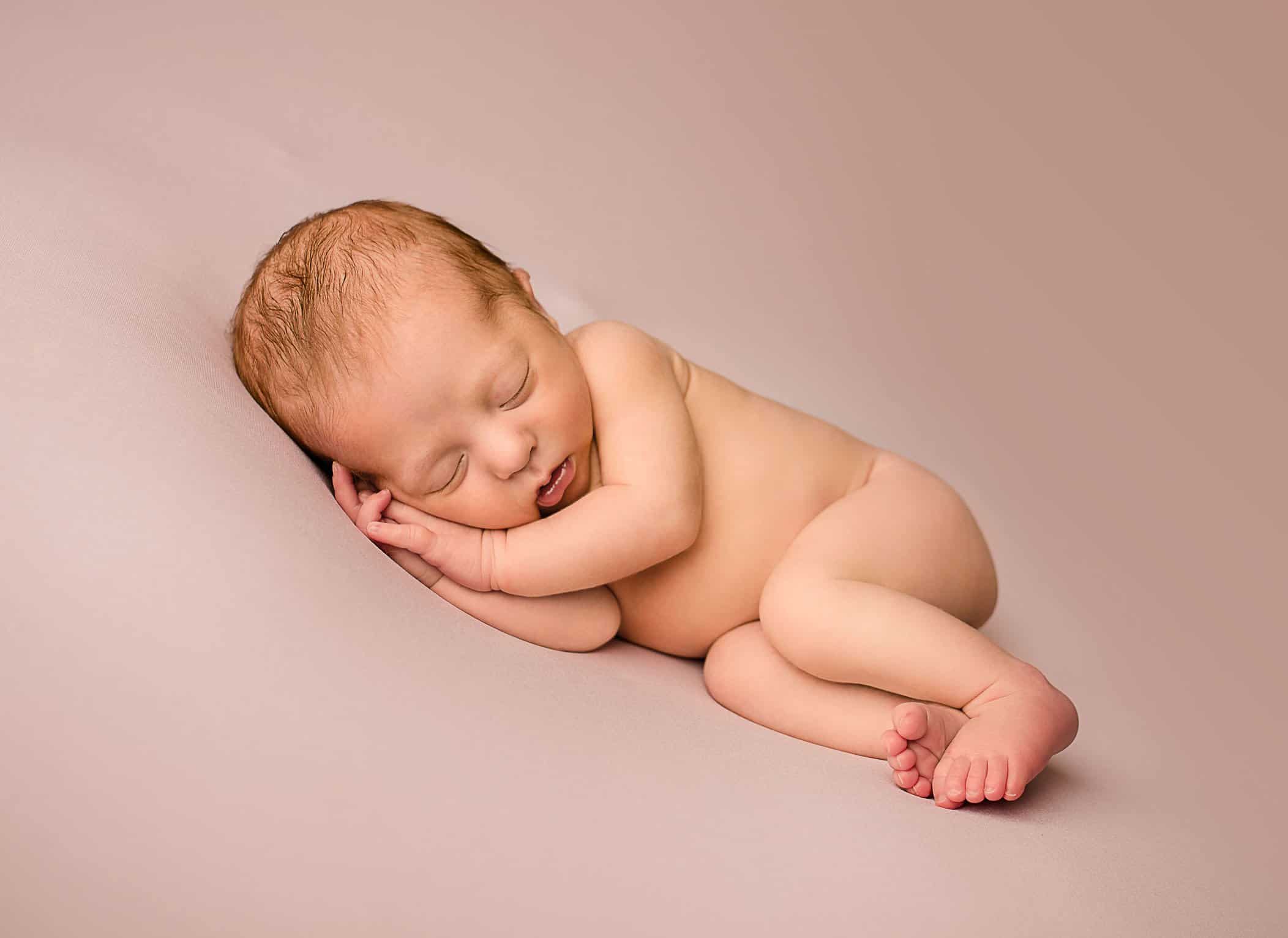 newborn baby girl sleeping naked on pink blanket with hands under her cheek