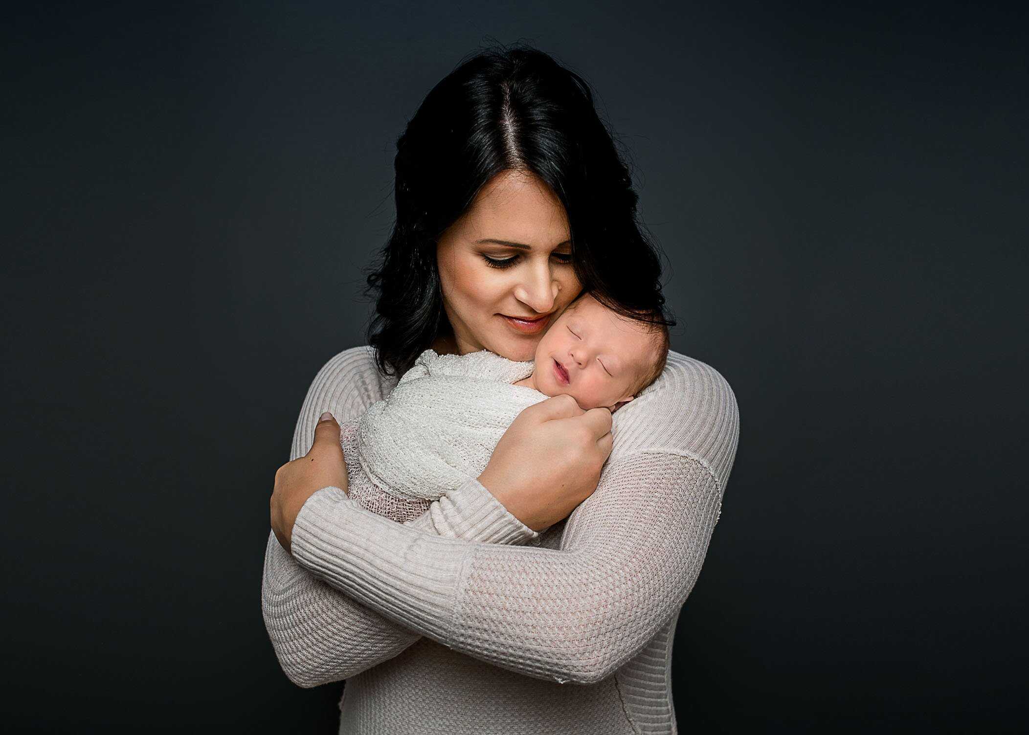mom cuddling newborn baby and both smiling
