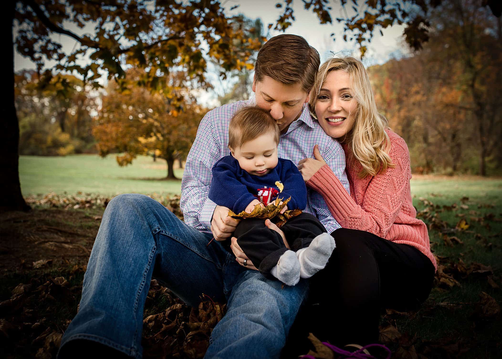 Mom snuggling Daddy while holding their baby boy outside in garden One Big HappyPhoto