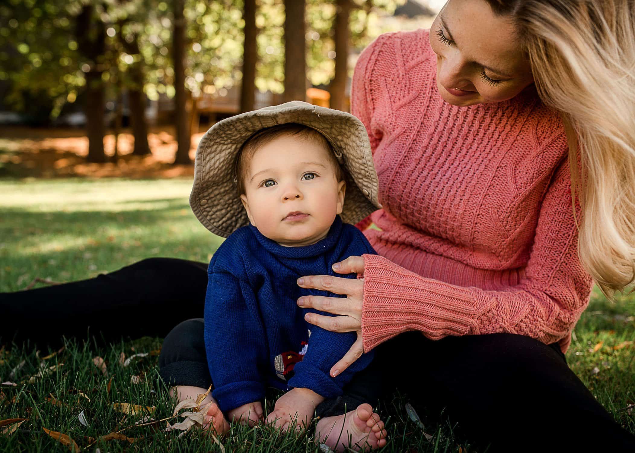 6 mo old baby boy sitting in grass with Mom with floppy hat on One Big Happy Photo