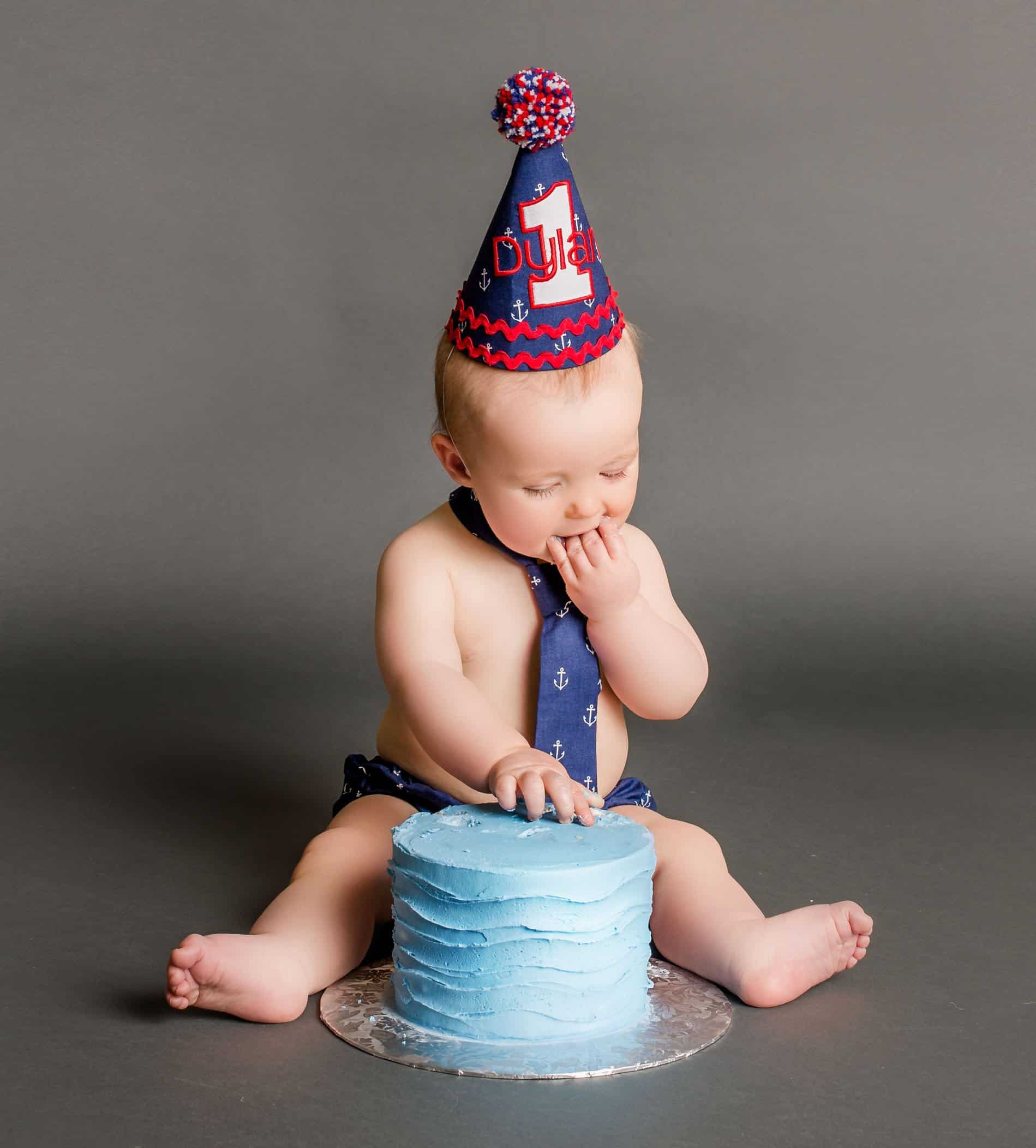 Baby with 1st birthday hat on eating his cake One Big Happy Photo