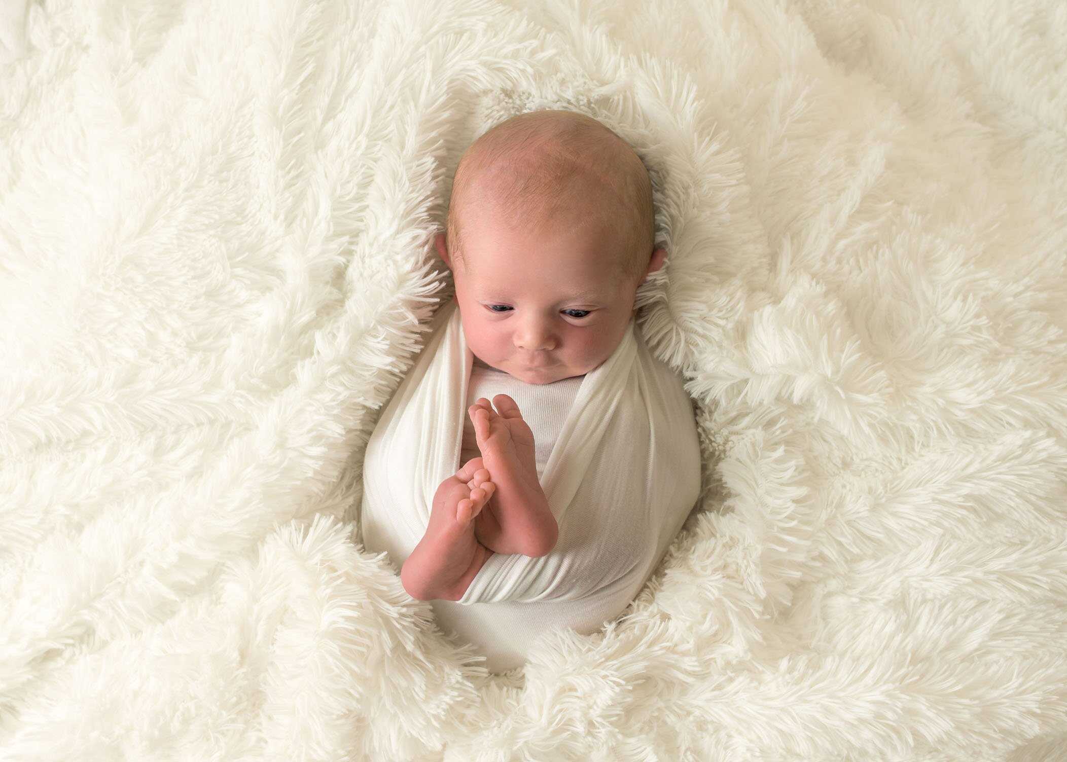 newborn baby awake wrapped in cream and looking at his toes One Big Happy Photo