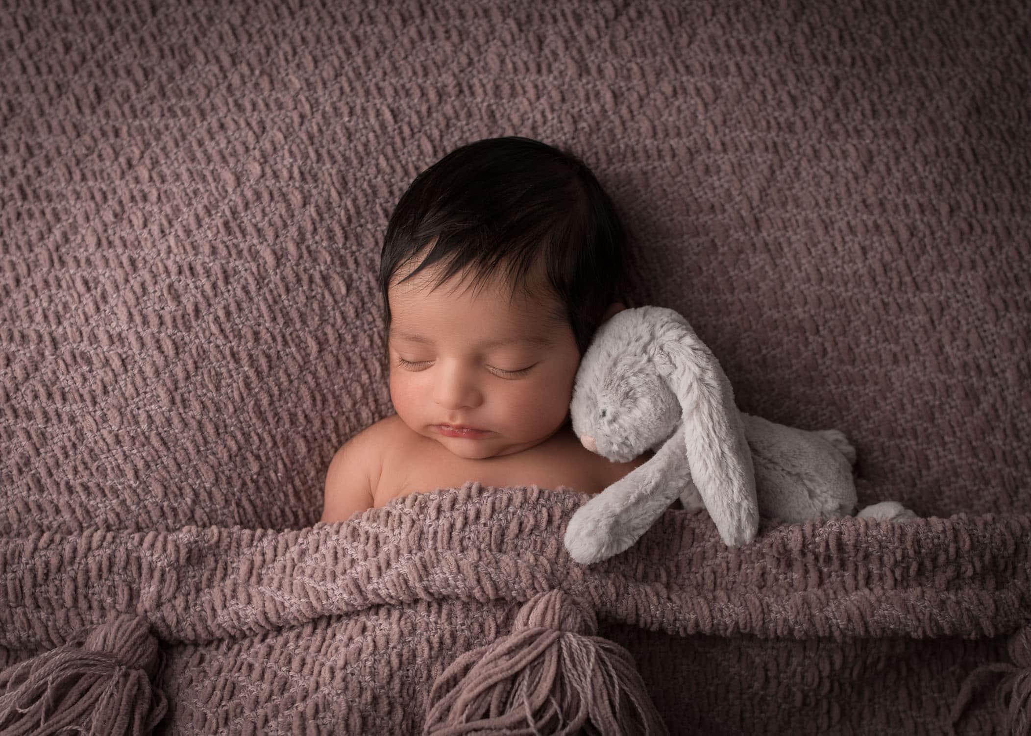 Newborn baby sleeping in bed with bunny cuddling her