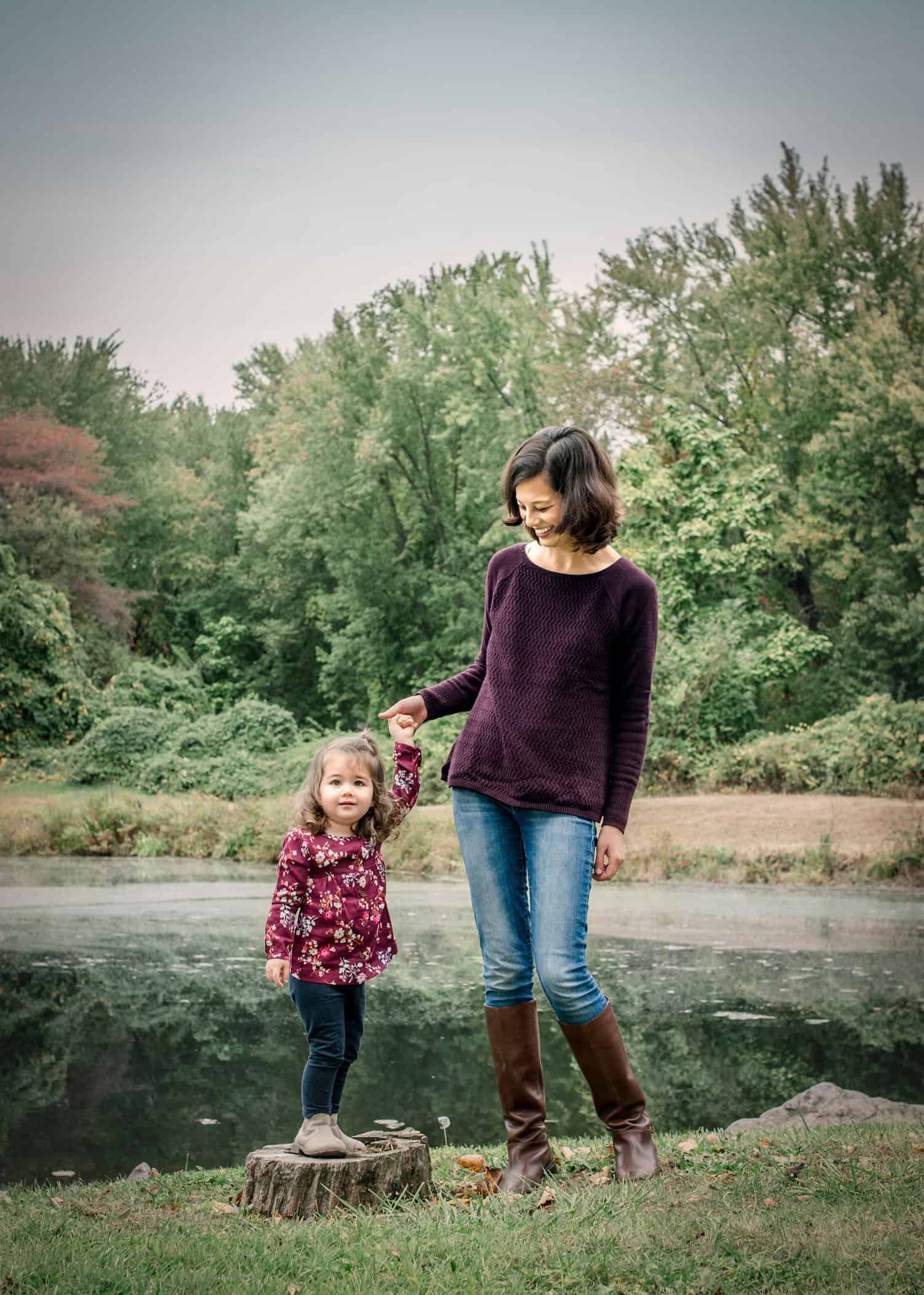 Mom holding 2 year old girl's hand outside by a pond
