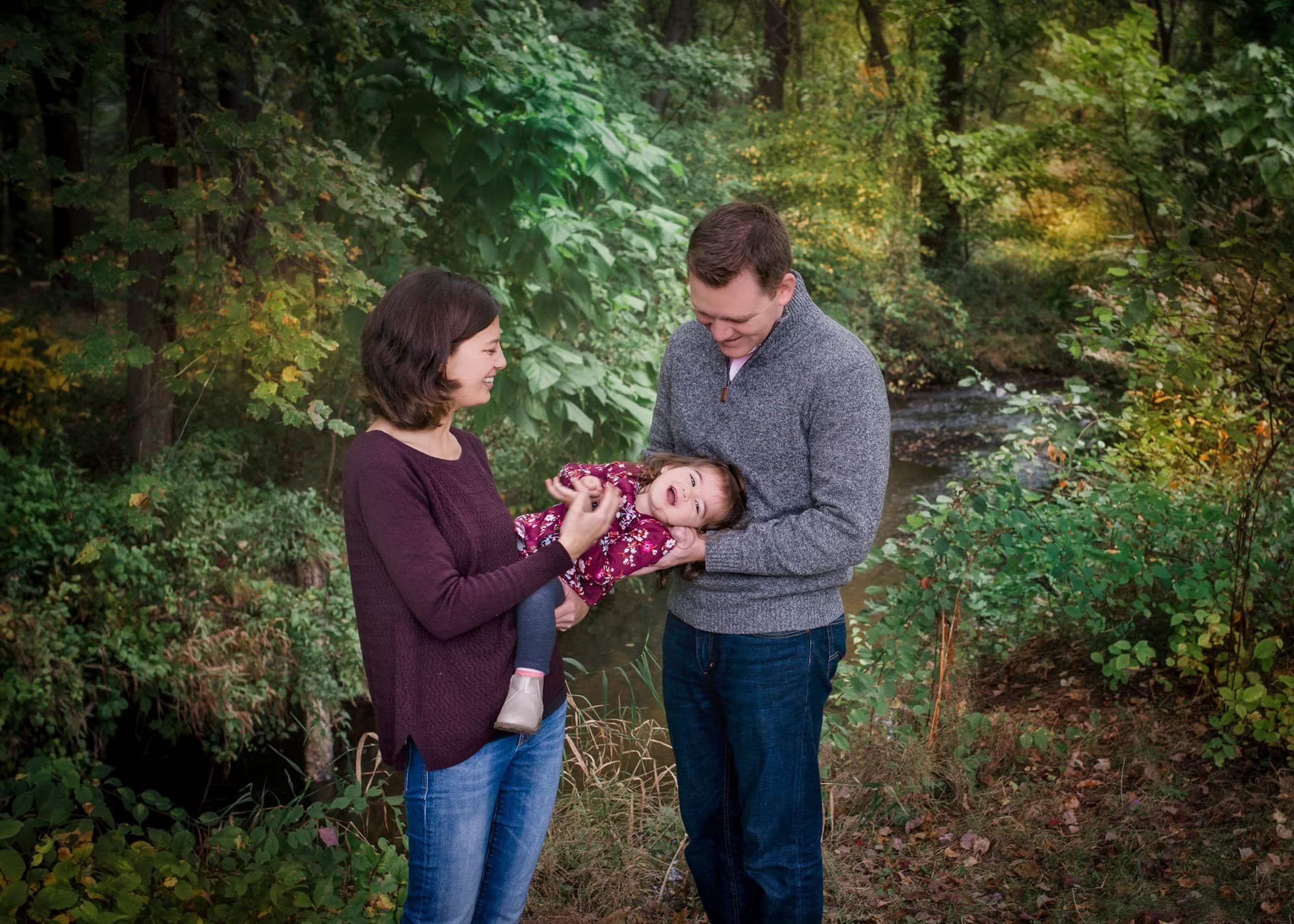 Mom and Dad tickling 2 year old girl outside in fall