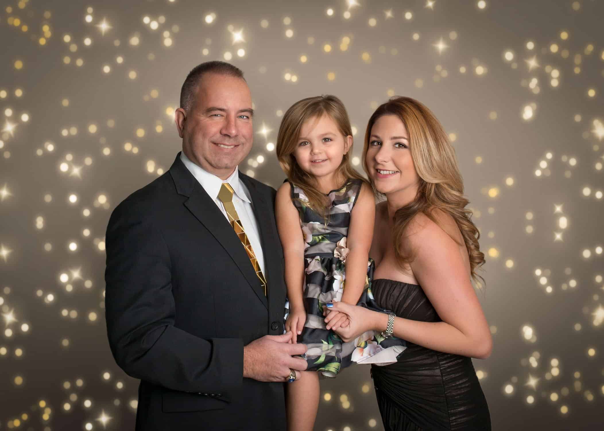 Mom and Dad holding their 3 year old daughter between them at a holiday party