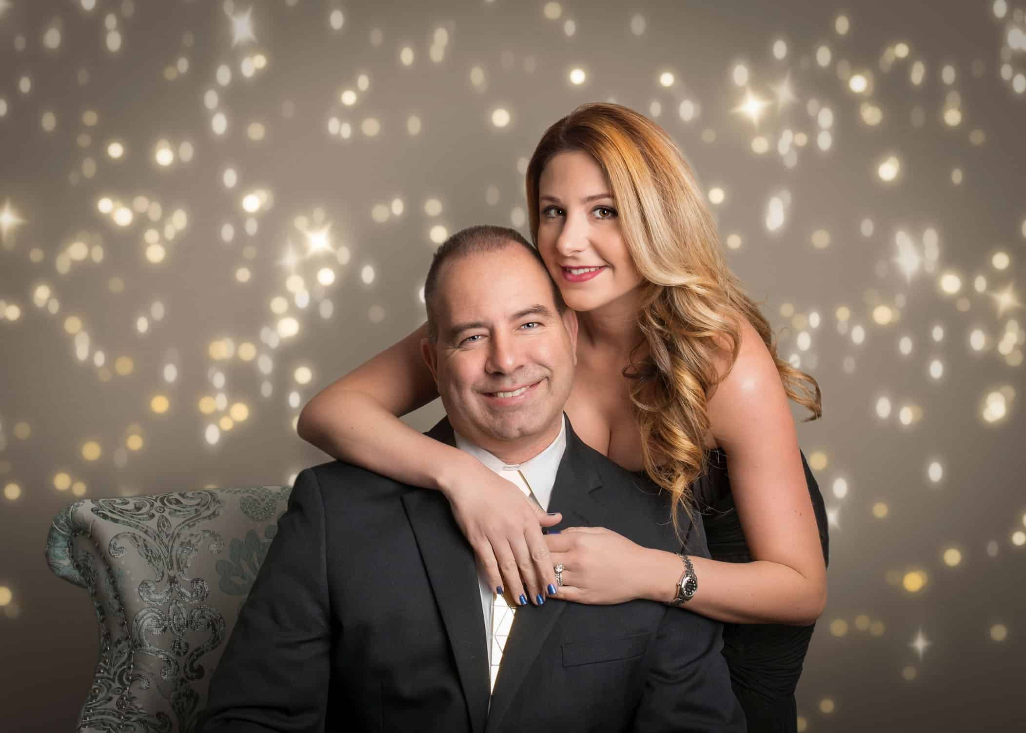 Mom giving Dad a hug over his shoulder with bokeh lights in the background
