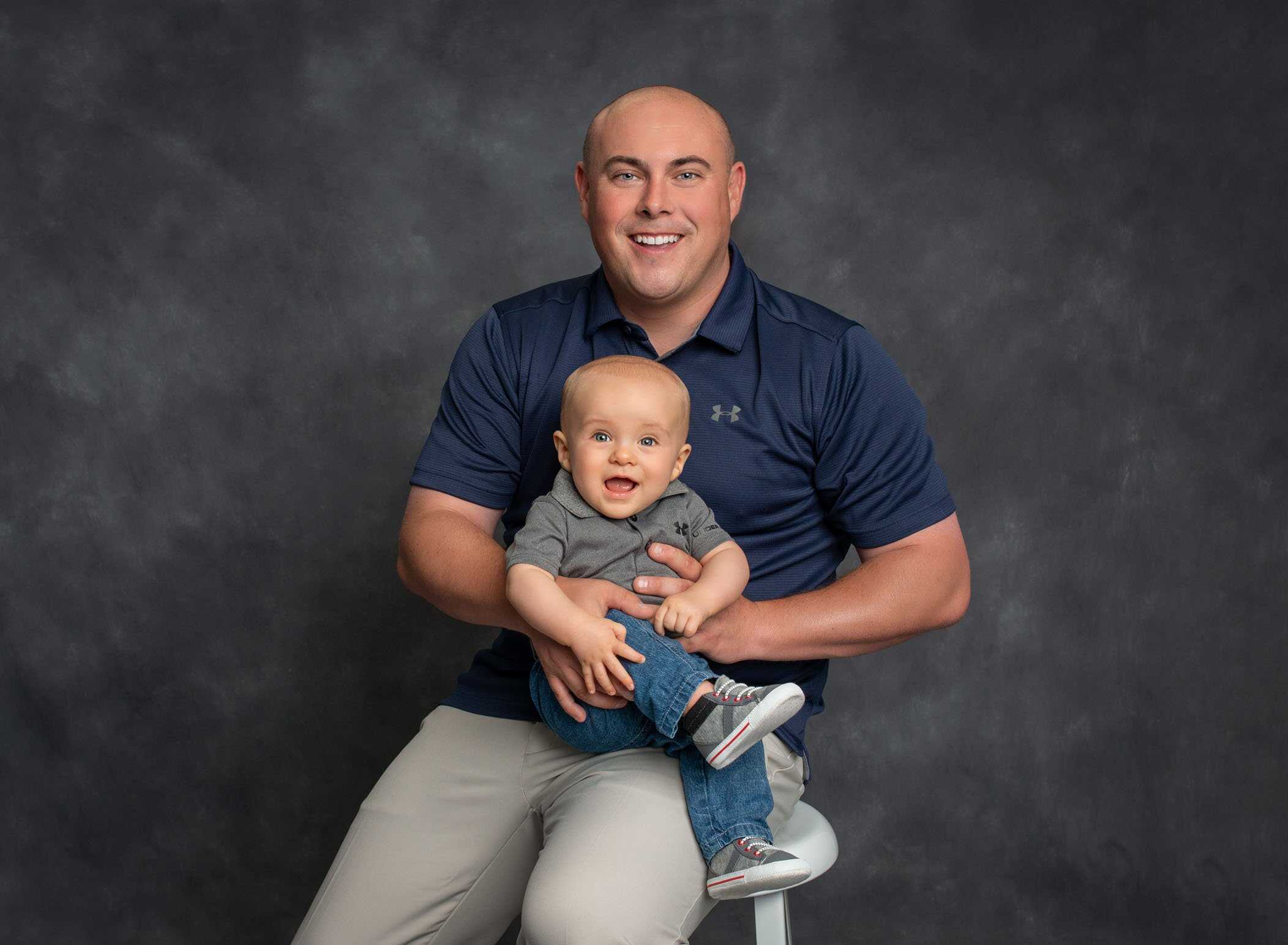 Dad holding 6 month old son on his lap and smiling