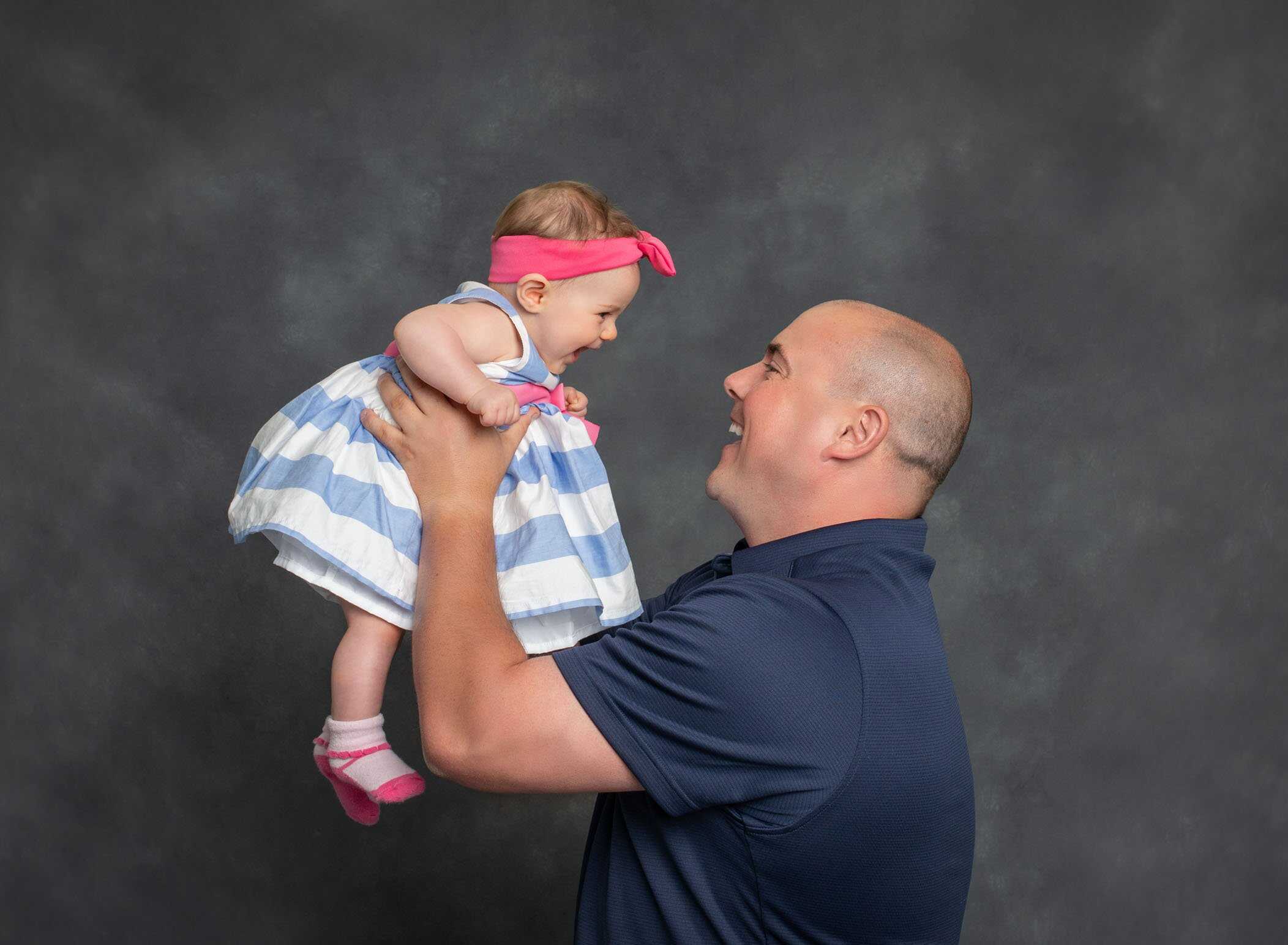 Dad holding 6 month old baby girl in the air and smiling