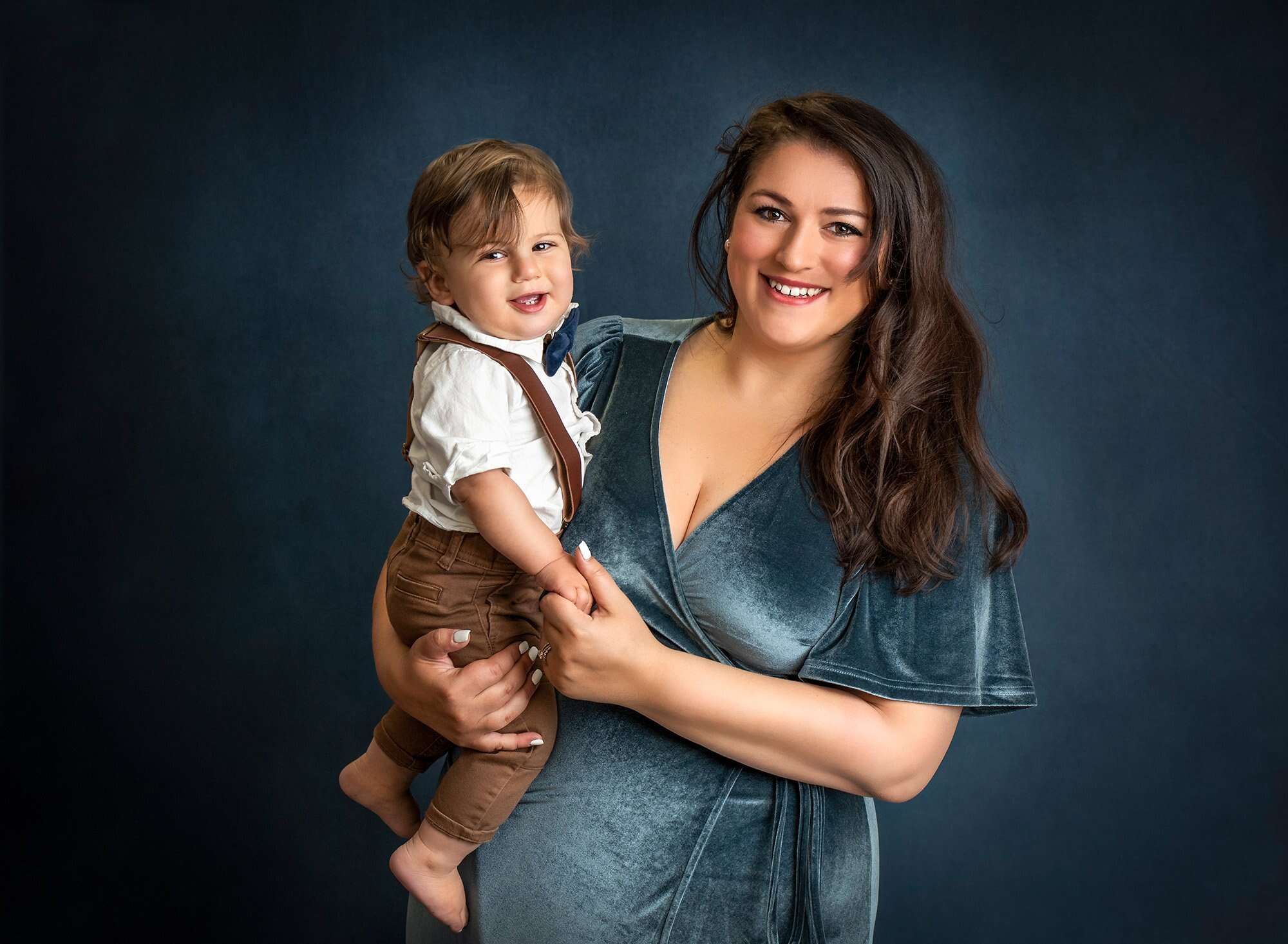 mom smiling as she holds her one year old boy smiling in overalls