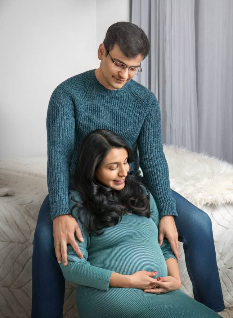 Expecting parents in teal sweaters embracing during maternity session