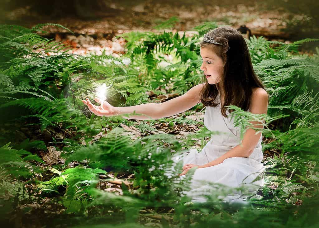little brown haired girl holding a fairy in her hand in the woods