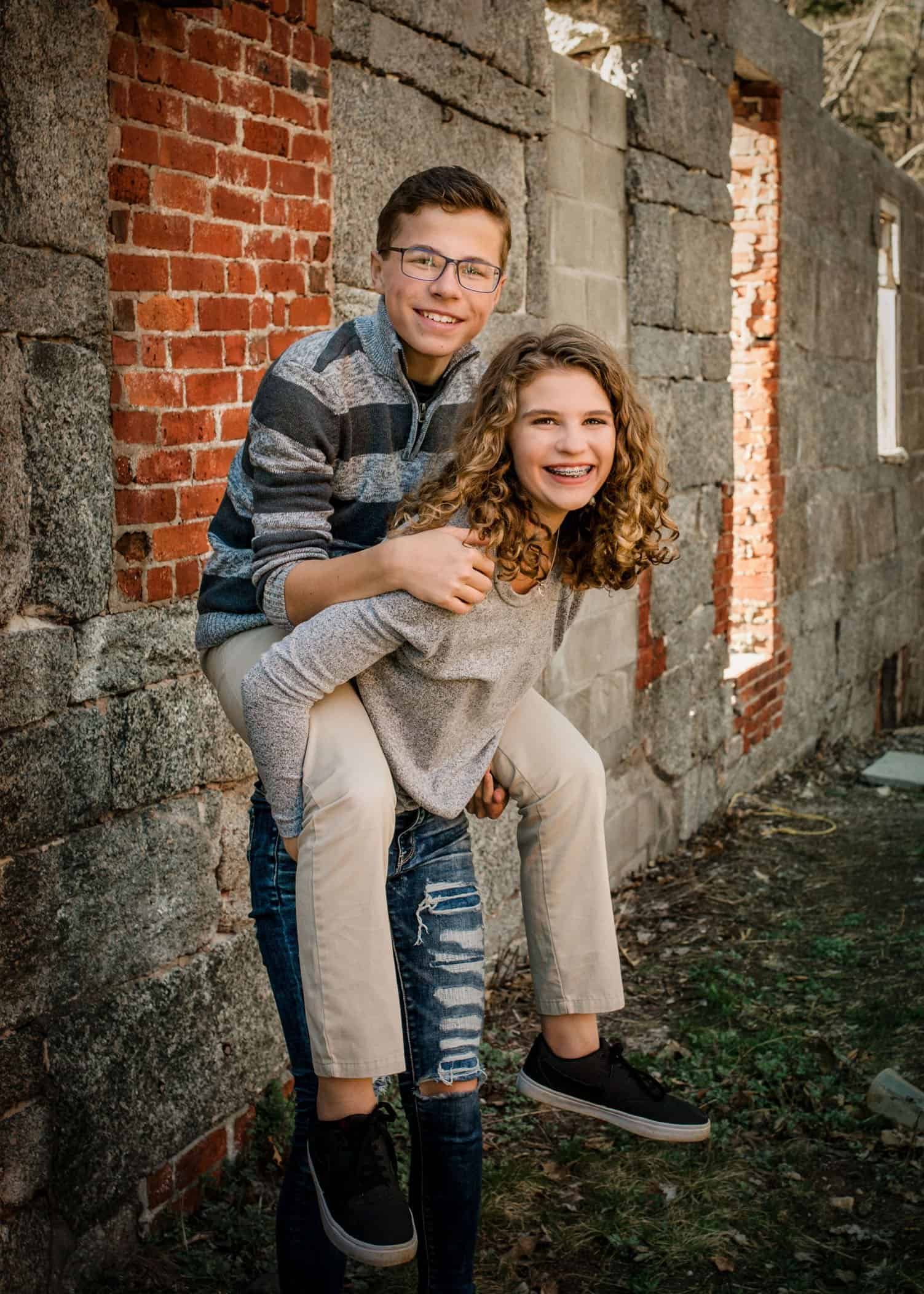 Younger brother climbs on big sisters back laughing outside at park