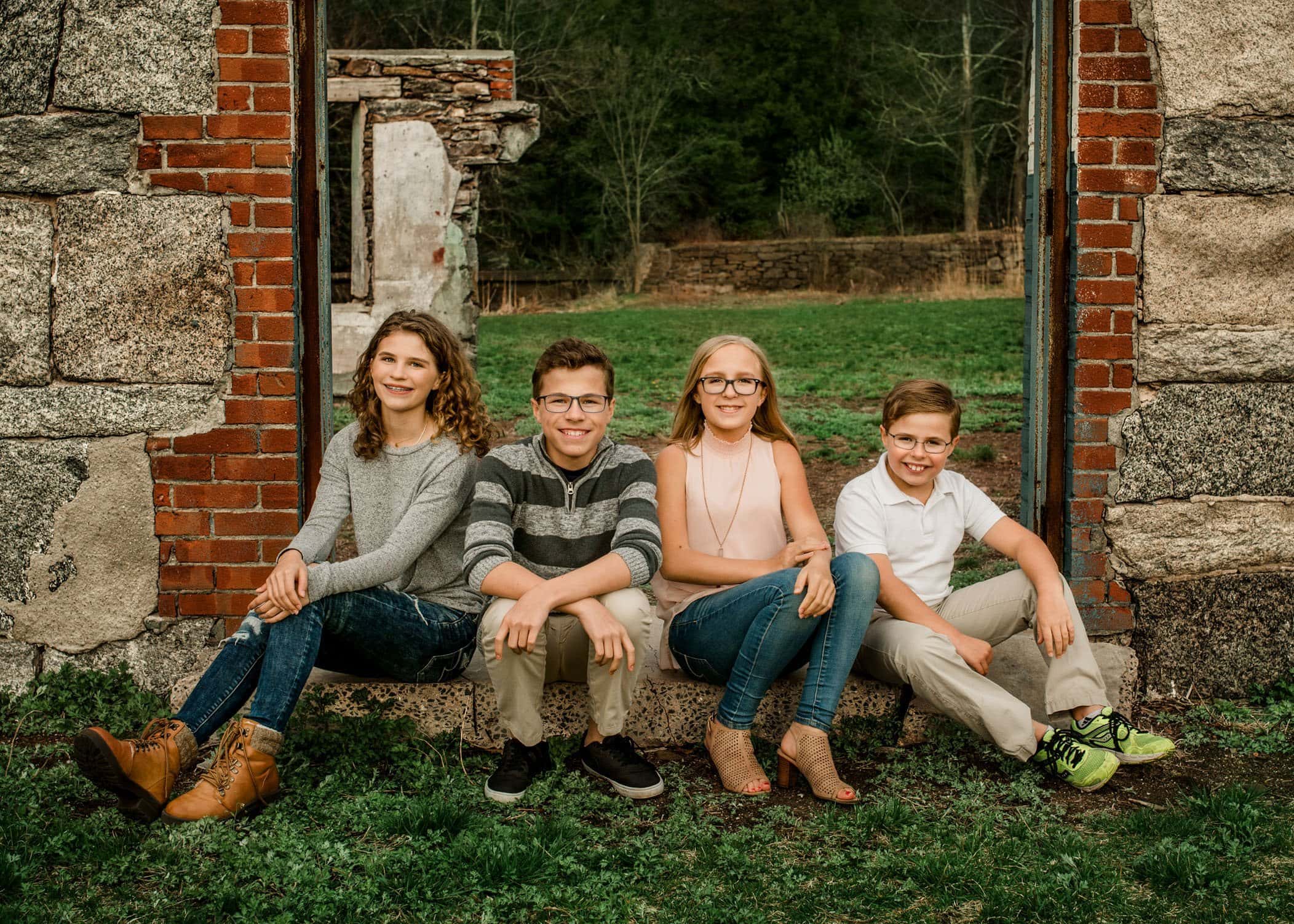 Four siblings sit outside on step of building ruins