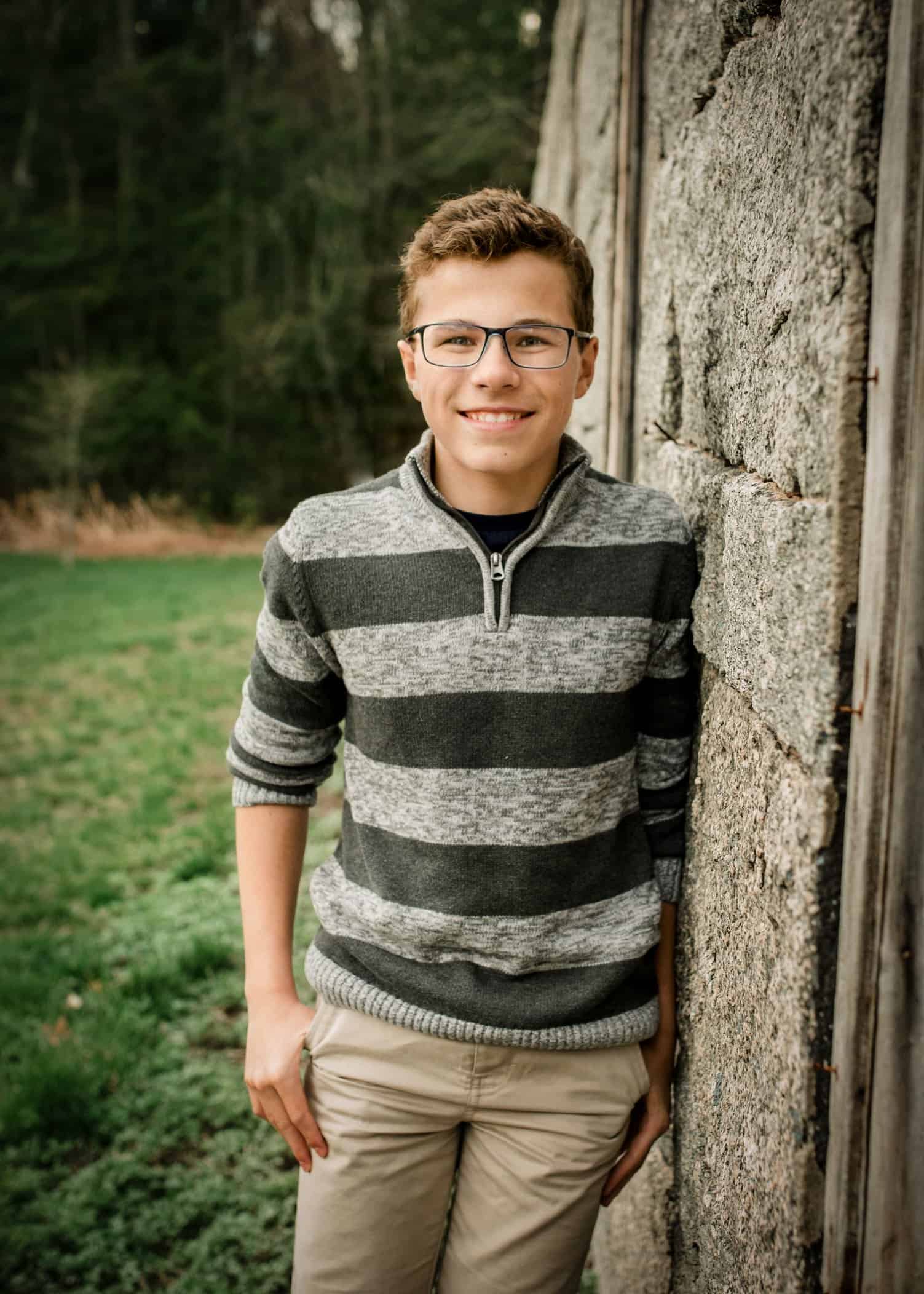 Tween boy leans against wall at building ruins outside smiling