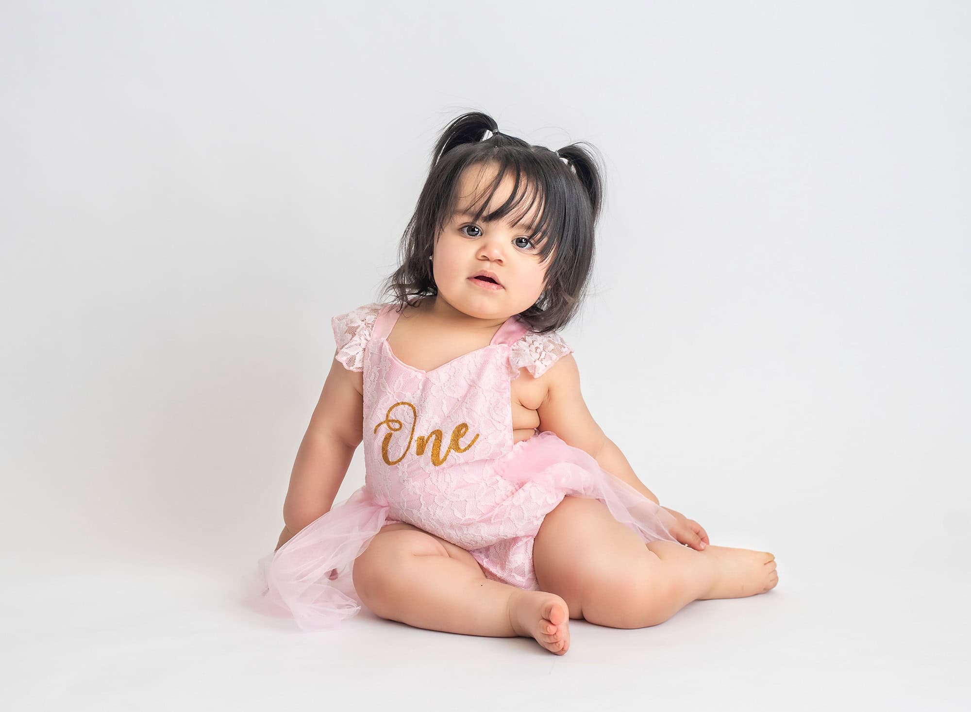 Butterfly Cake Smash Pictures one year old baby girl in pigtails and pink laced one dress on neutral background