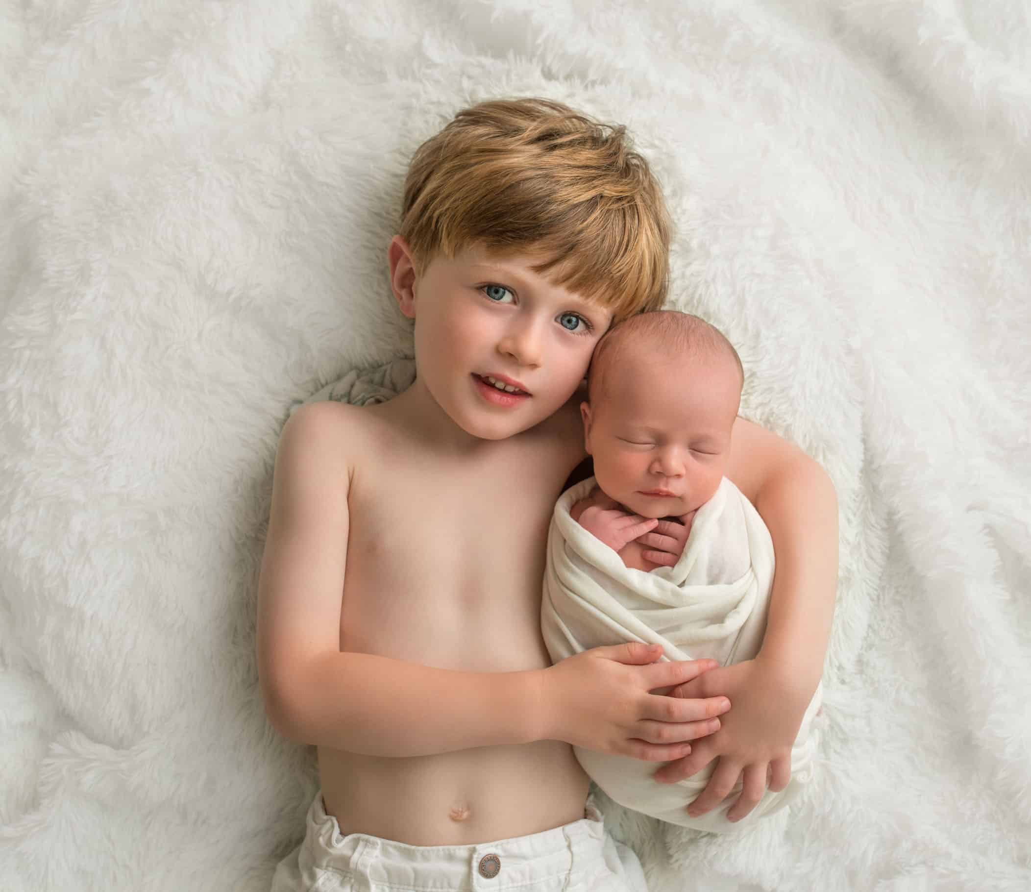 4 year old brother snuggling with newborn baby sister on cream rug