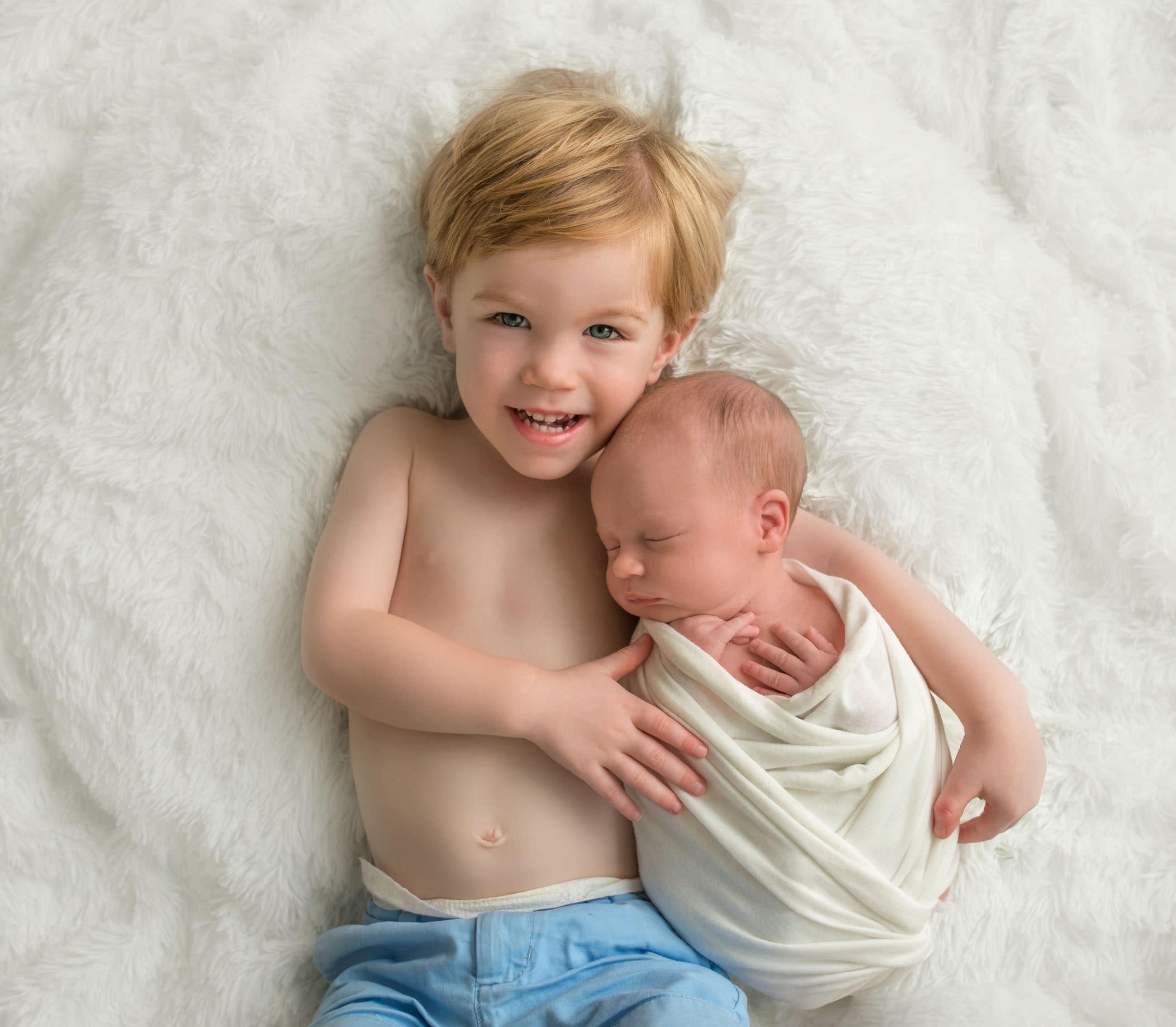 2 year old brother snuggling with newborn baby sister on cream rug