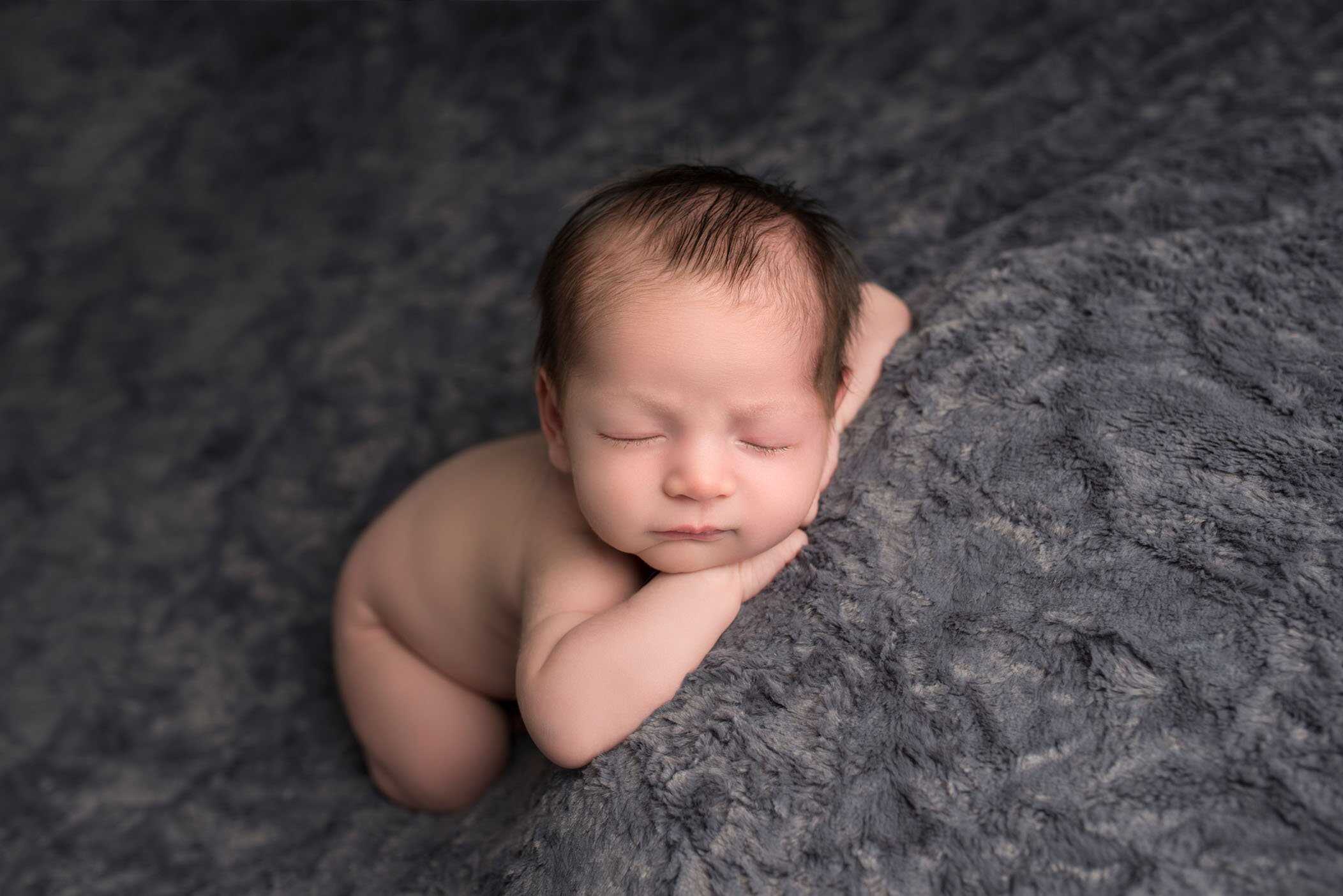 newborn baby boy sleeping on grey with head on hands