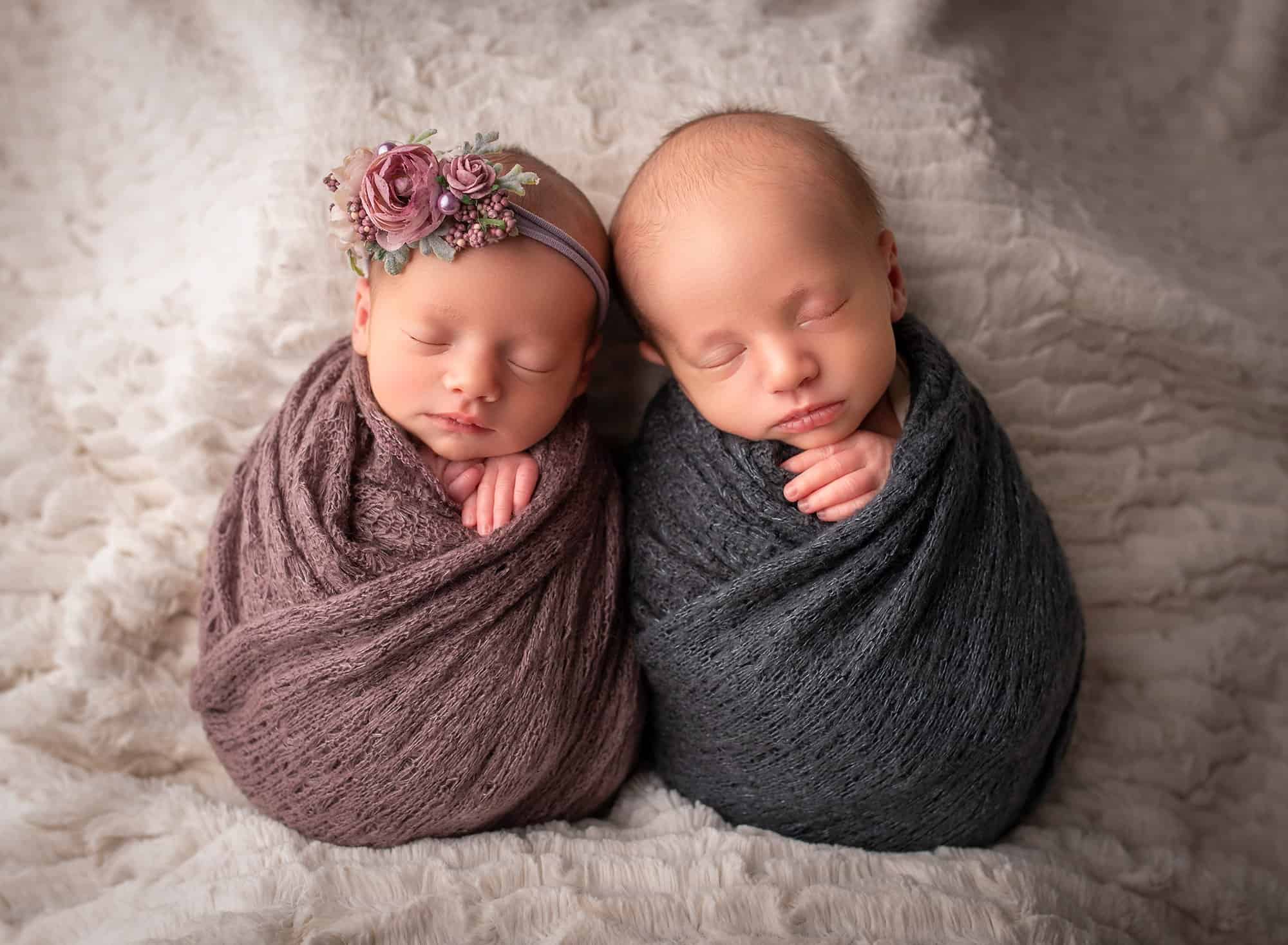 newborn twins asleep swaddled next to each other on fluffy blanket