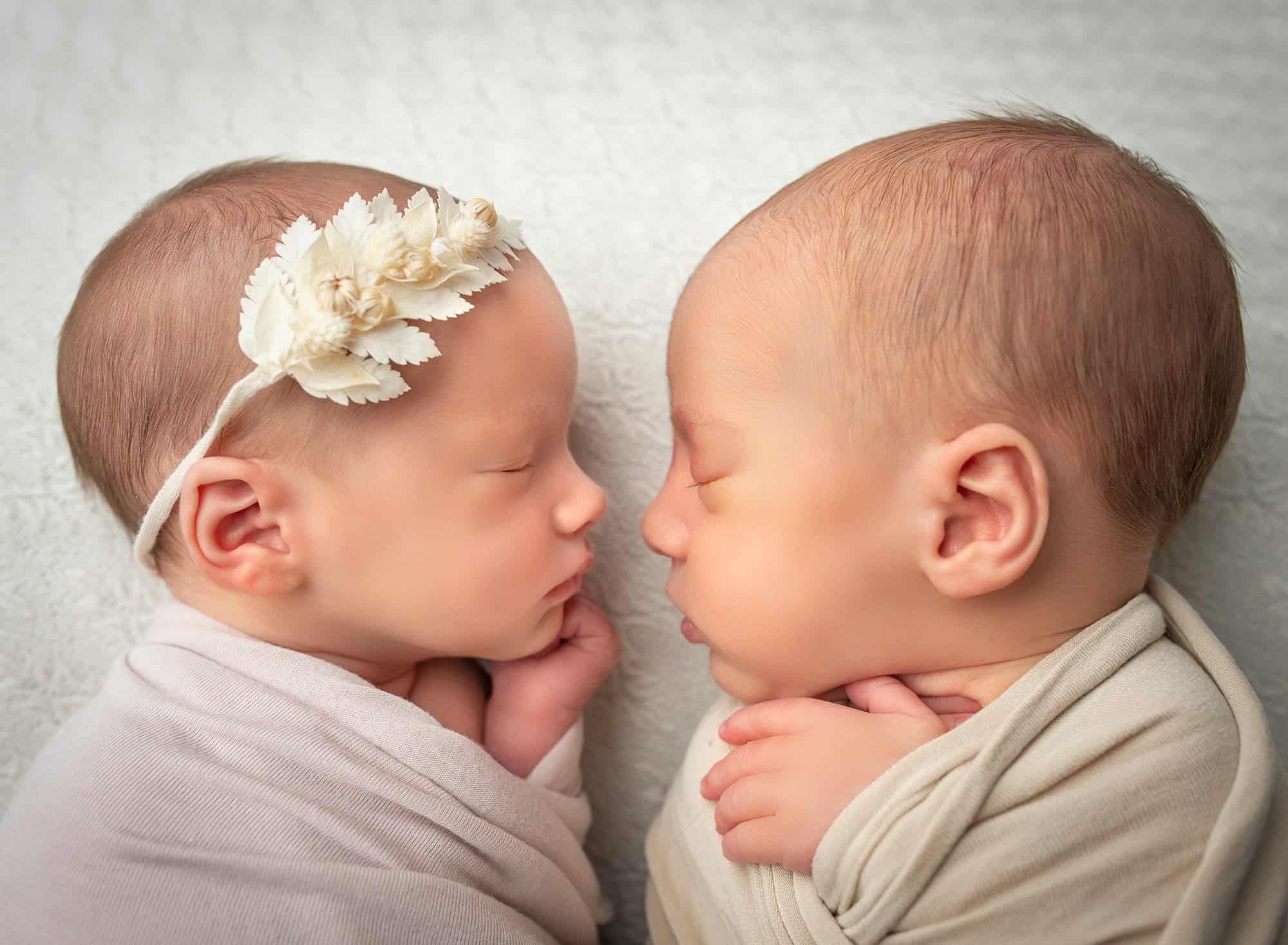 newborn twin girl and boy sound asleep facing each other swaddled in wraps