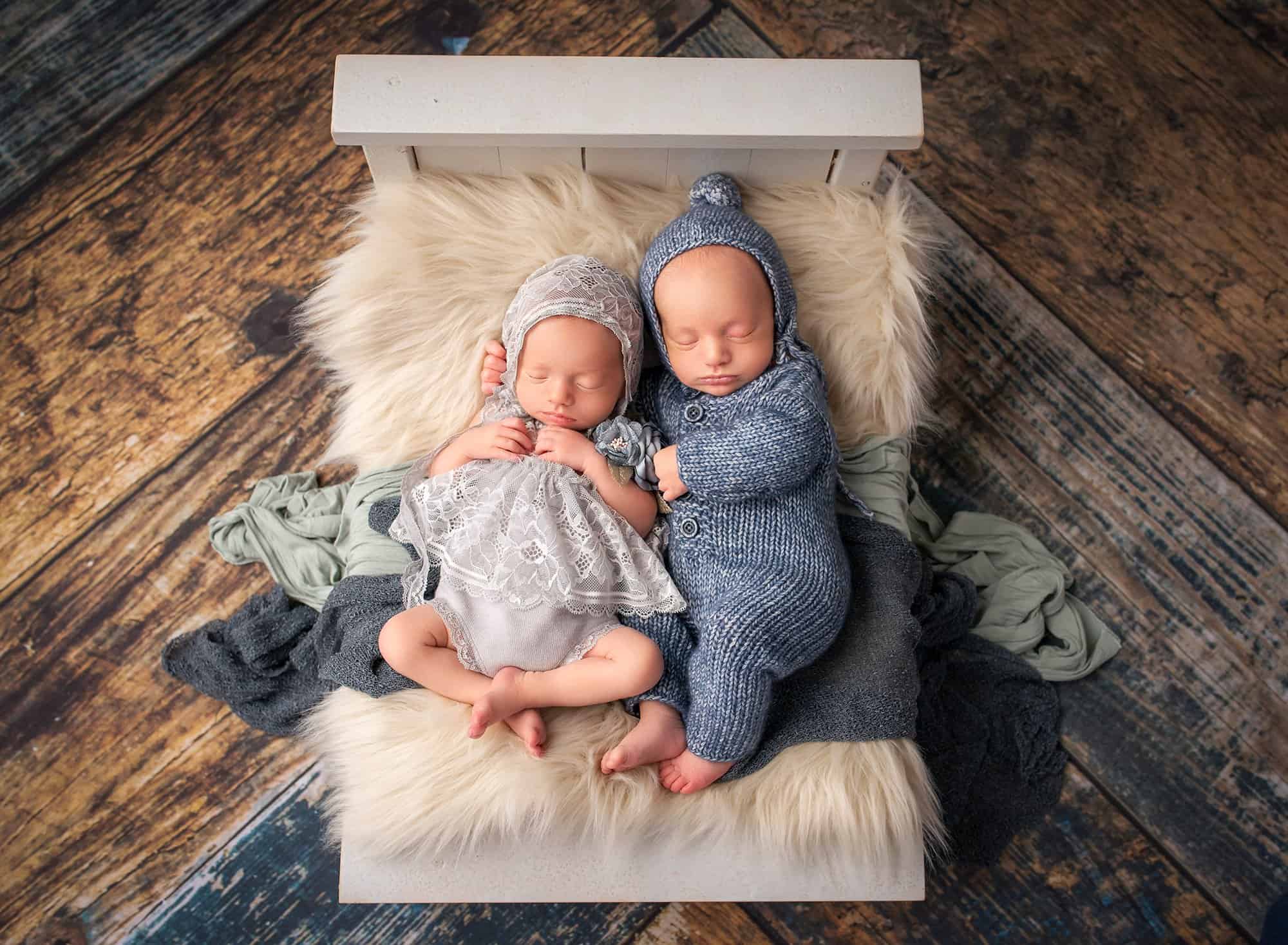 Twins newborn photography newborn twin boy and girl laying asleep next to each other on a miniature white bed with blankets