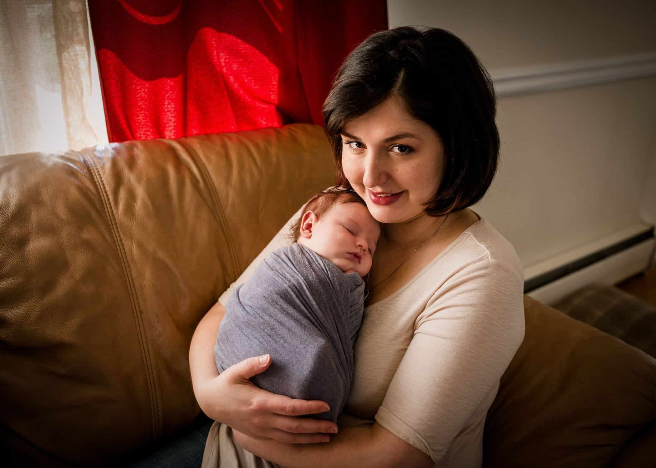 Mom holding her newborn son against her chest and looking at camera